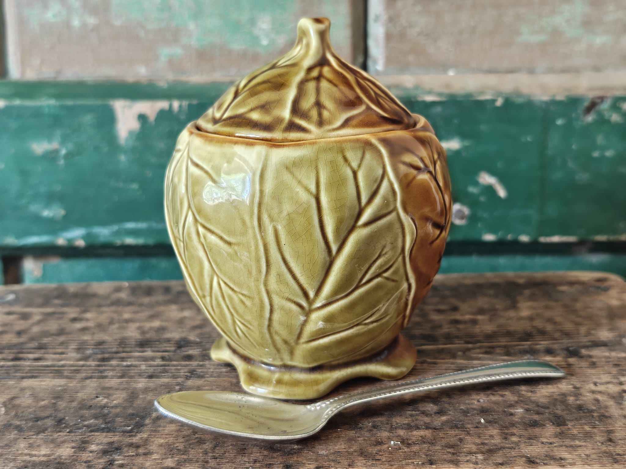A ceramic lidded container with a leaf-like embossed pattern in a warm olive-gold glaze.
