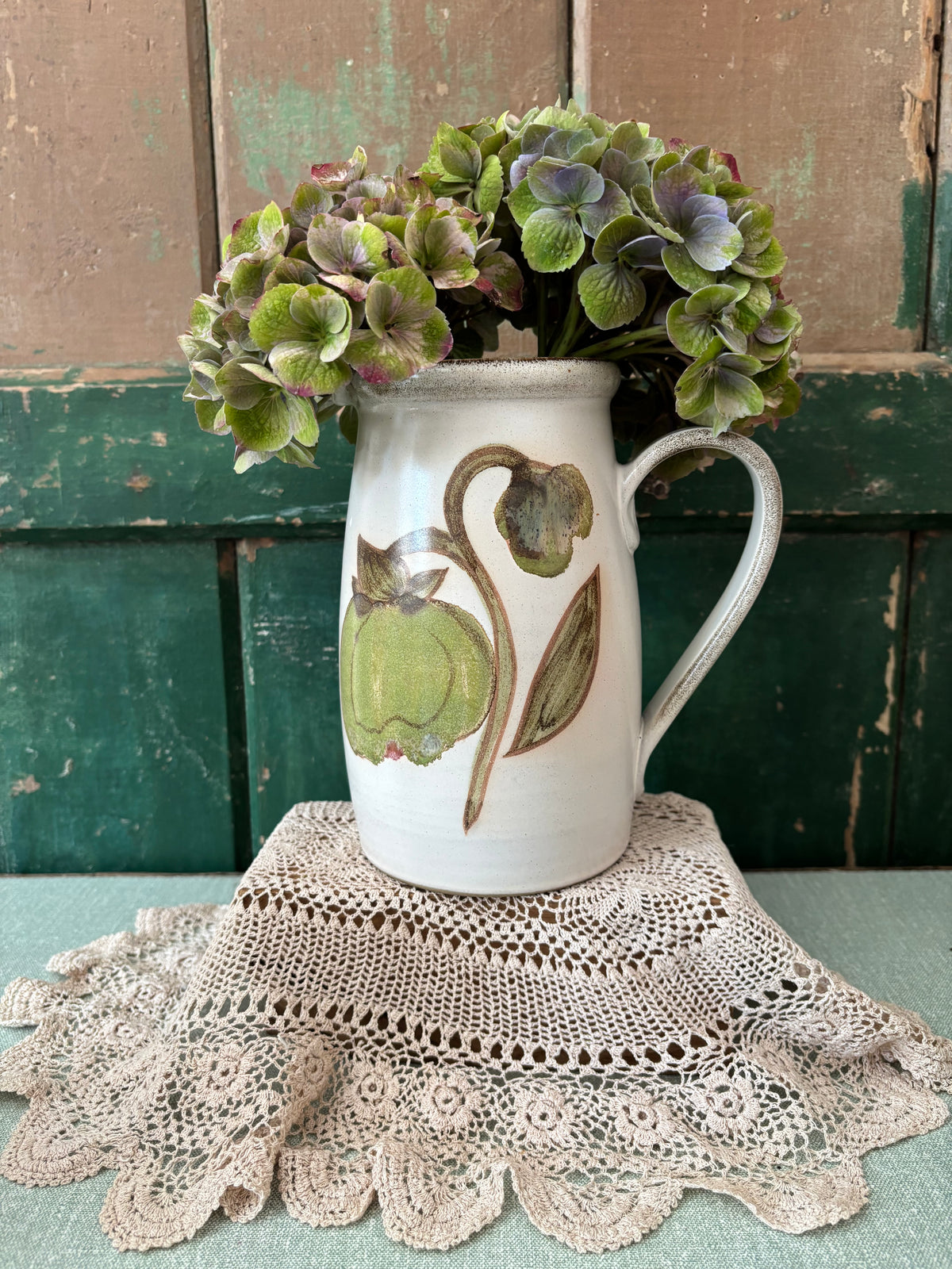 A white ceramic pitcher vase with a painted green magnolia bud design.