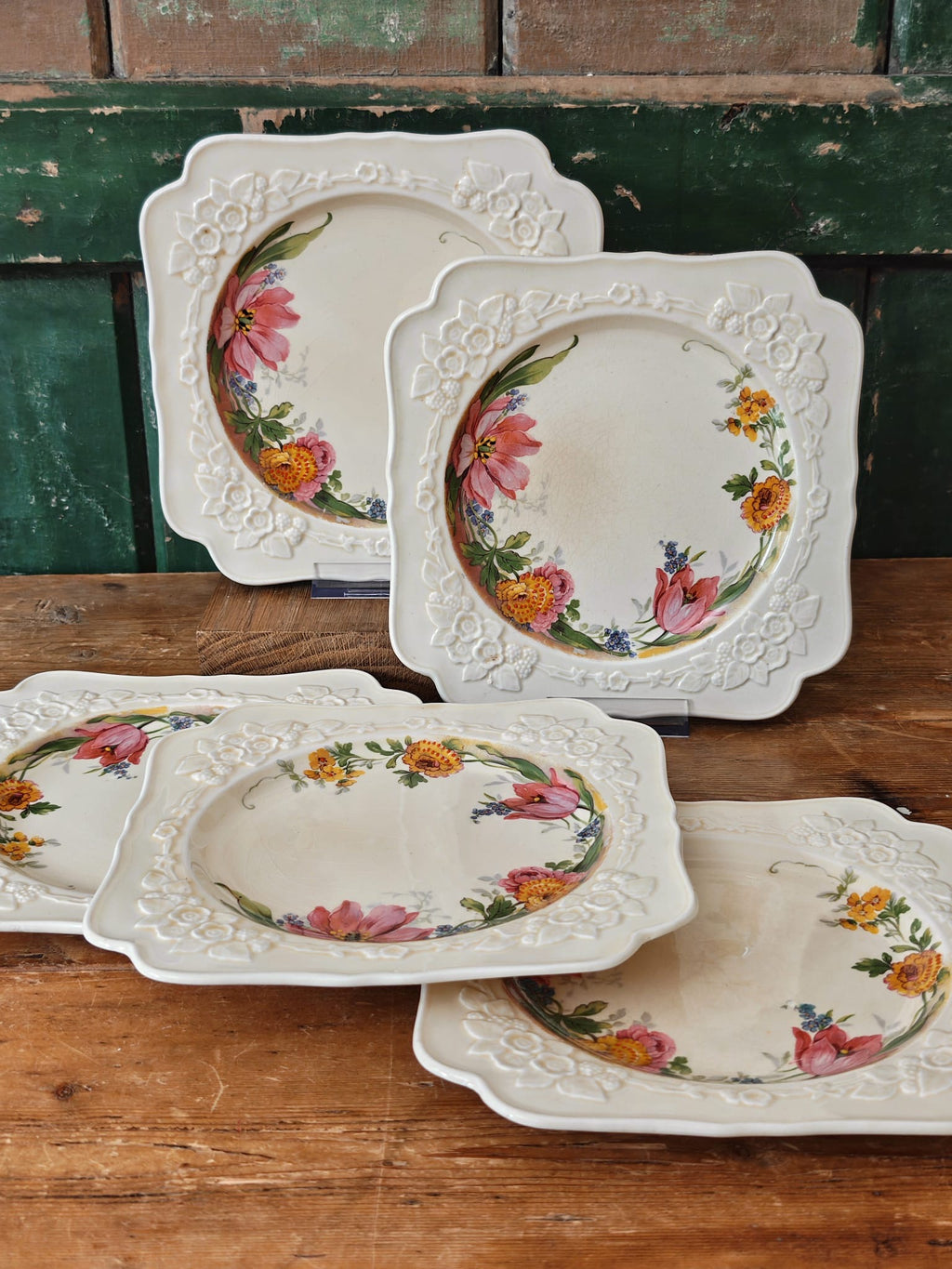 A set of vintage ceramic plates with embossed floral borders and painted pink flowers.