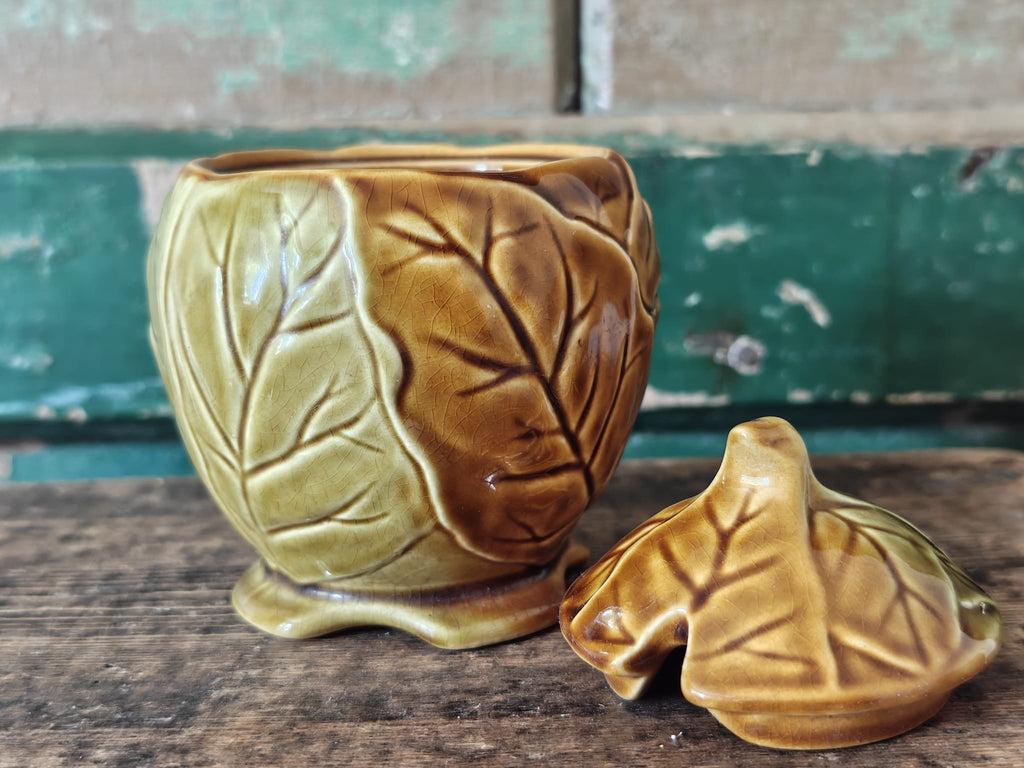 A ceramic lidded container with a leaf-like embossed pattern in a warm olive-gold glaze showing the lid by the side.