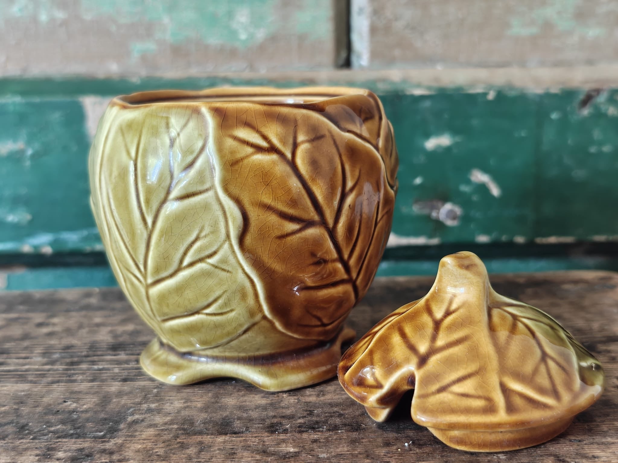 A ceramic lidded container with a leaf-like embossed pattern in a warm olive-gold glaze showing the lid by the side.