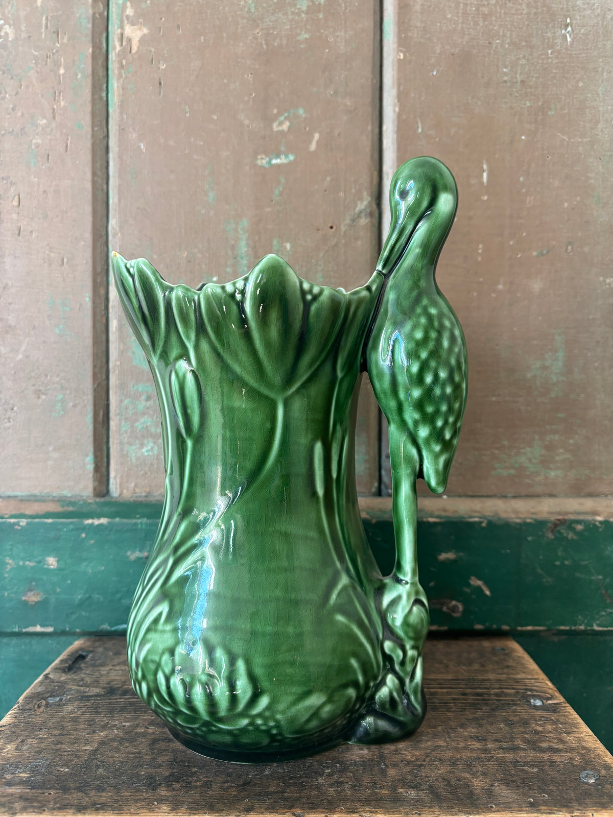 A dark green ceramic vase shaped like a lotus flower with a sculpted heron figure rising from the right side.
