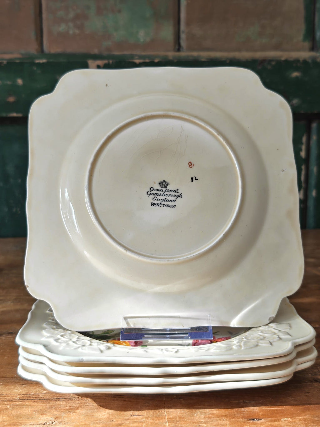 A stack of vintage white ceramic plates with scalloped edges, showing the inner printed brand mark 'Crown Ducal'.