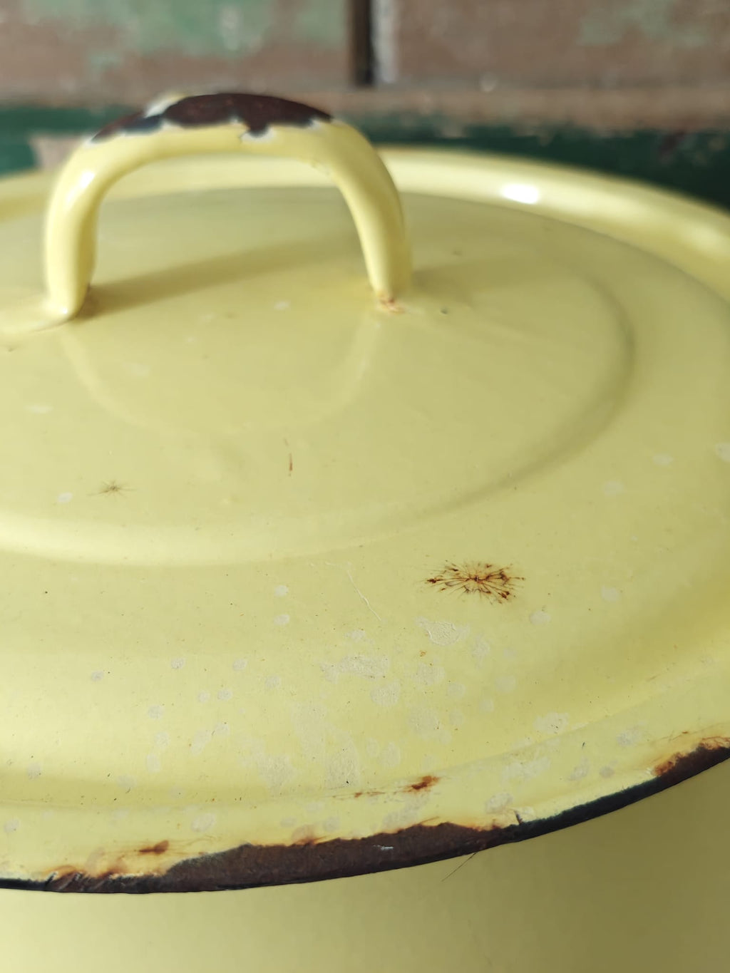 Yellow enameled pot with a lid showing signs of wear and rust.