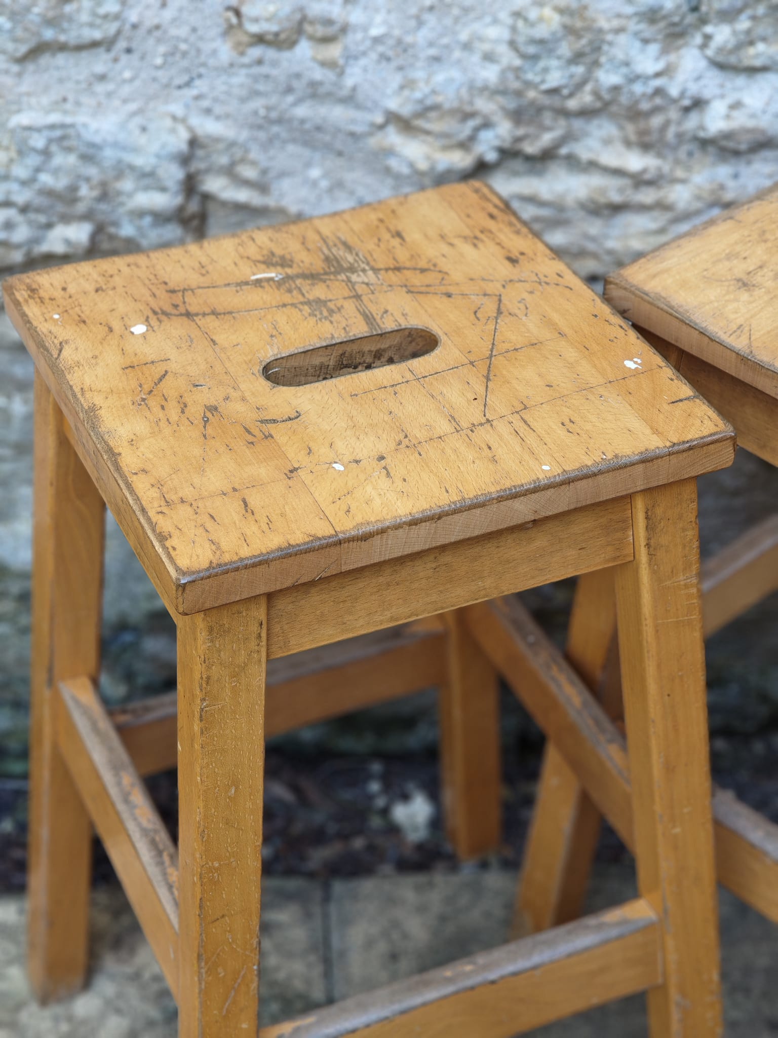 A rustic wooden stool with a square seat featuring a central cutout