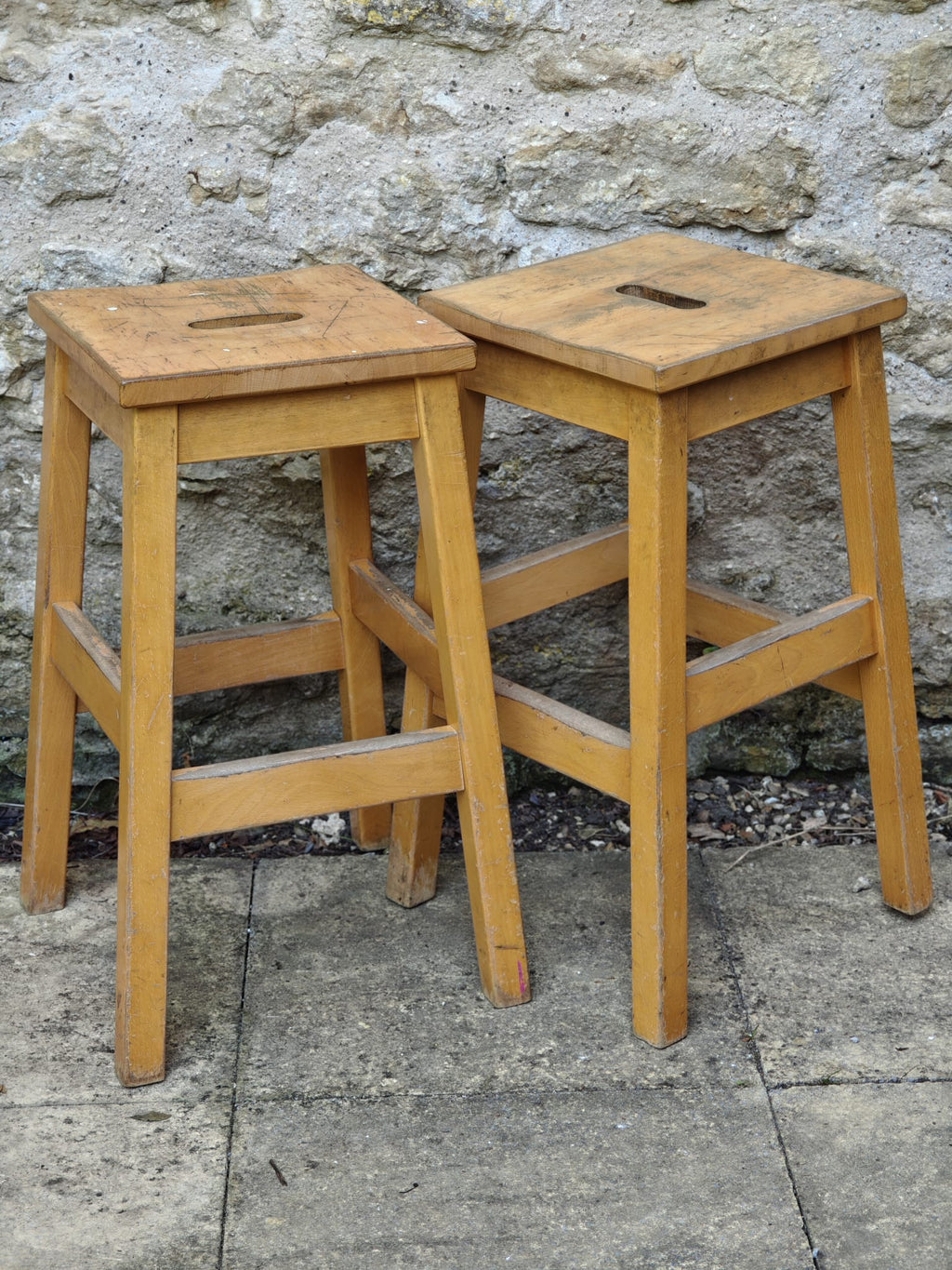 Two light natural wood bar stools with square seats.