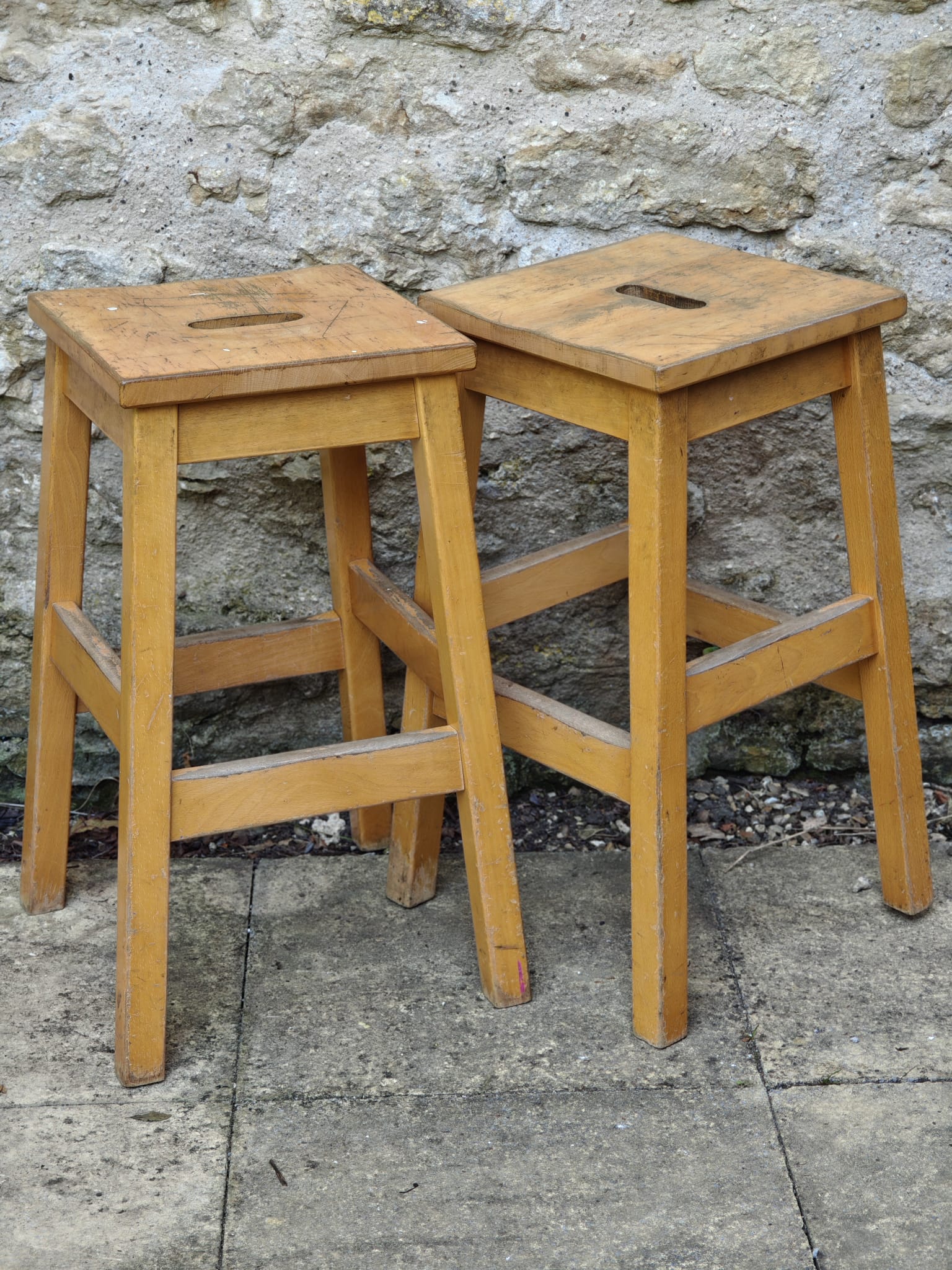 Two light natural wood bar stools with square seats.