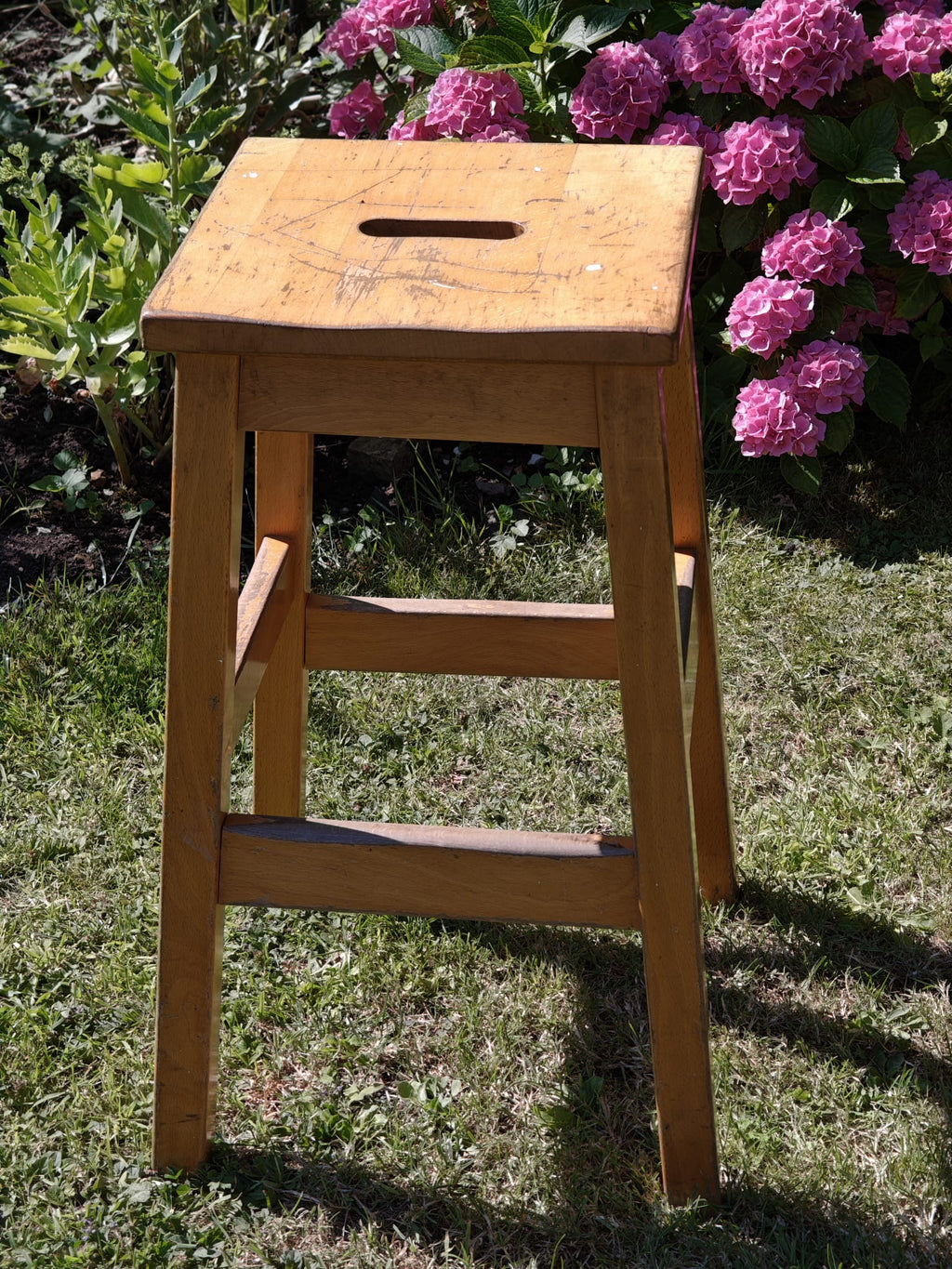 A rustic wooden stool with a square seat and a central cutout handle.
