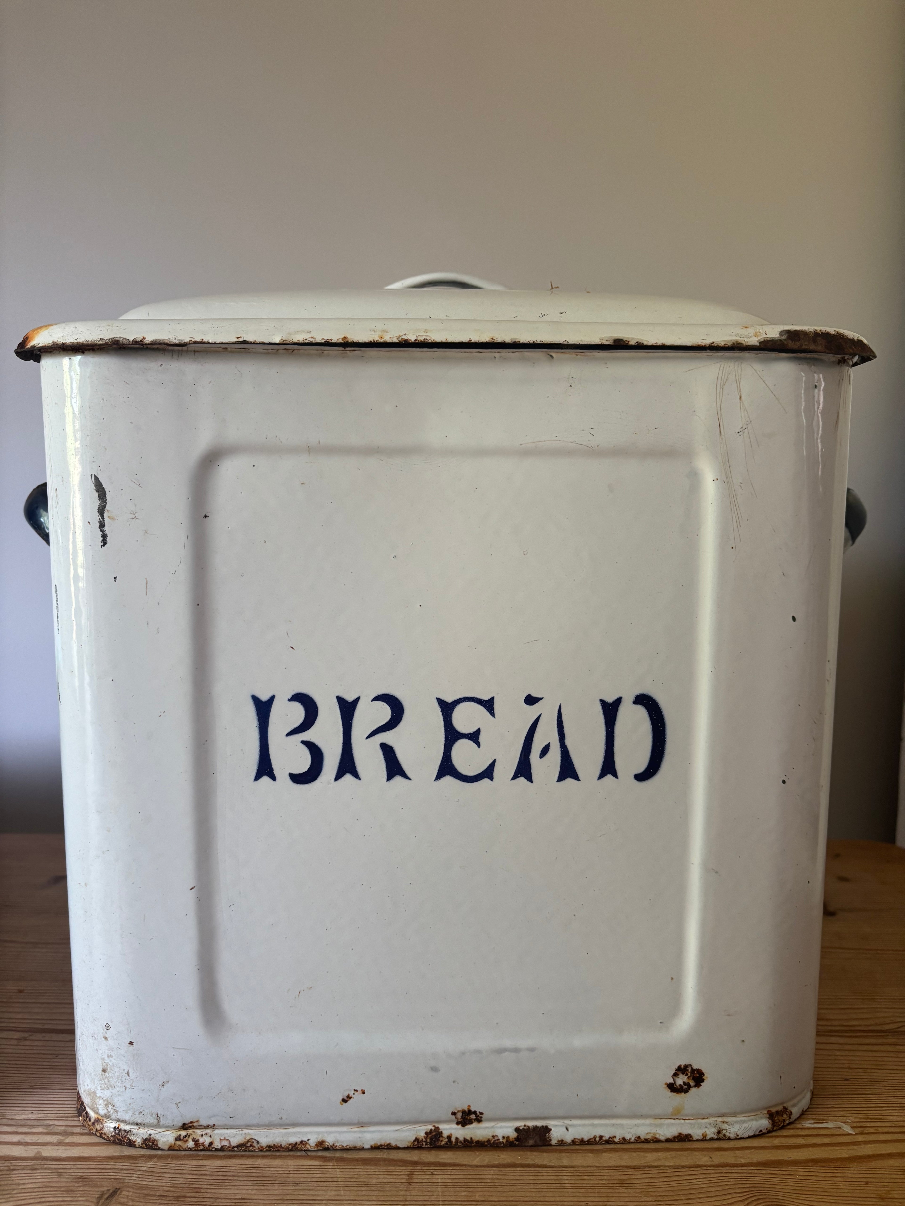 A vintage white enamel bread bin with a lid, featuring the word 'BREAD' printed in dark blue on the front. 