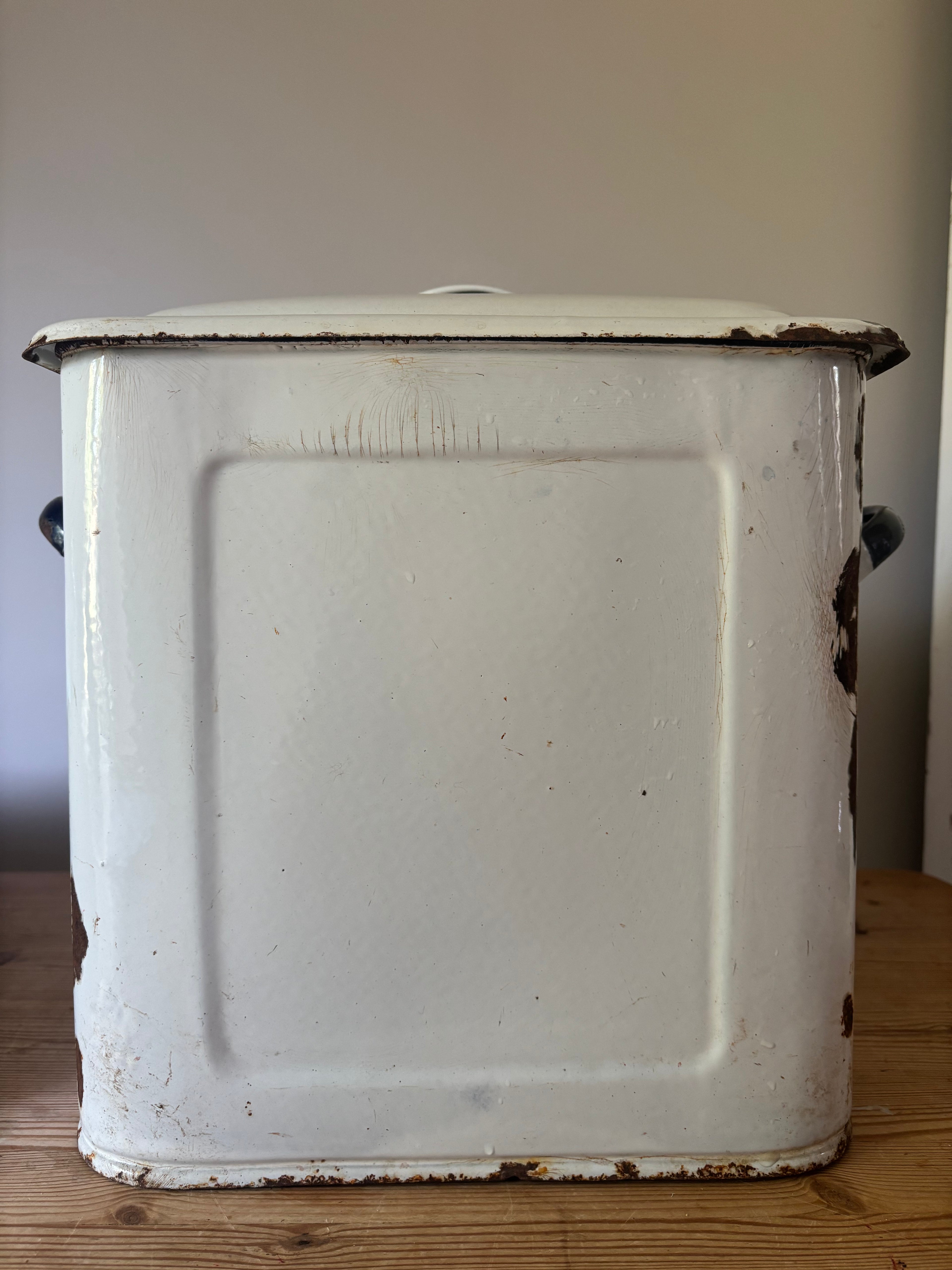 A vintage white enamel metal storage box with a lid, showing rust and wear on the edges.