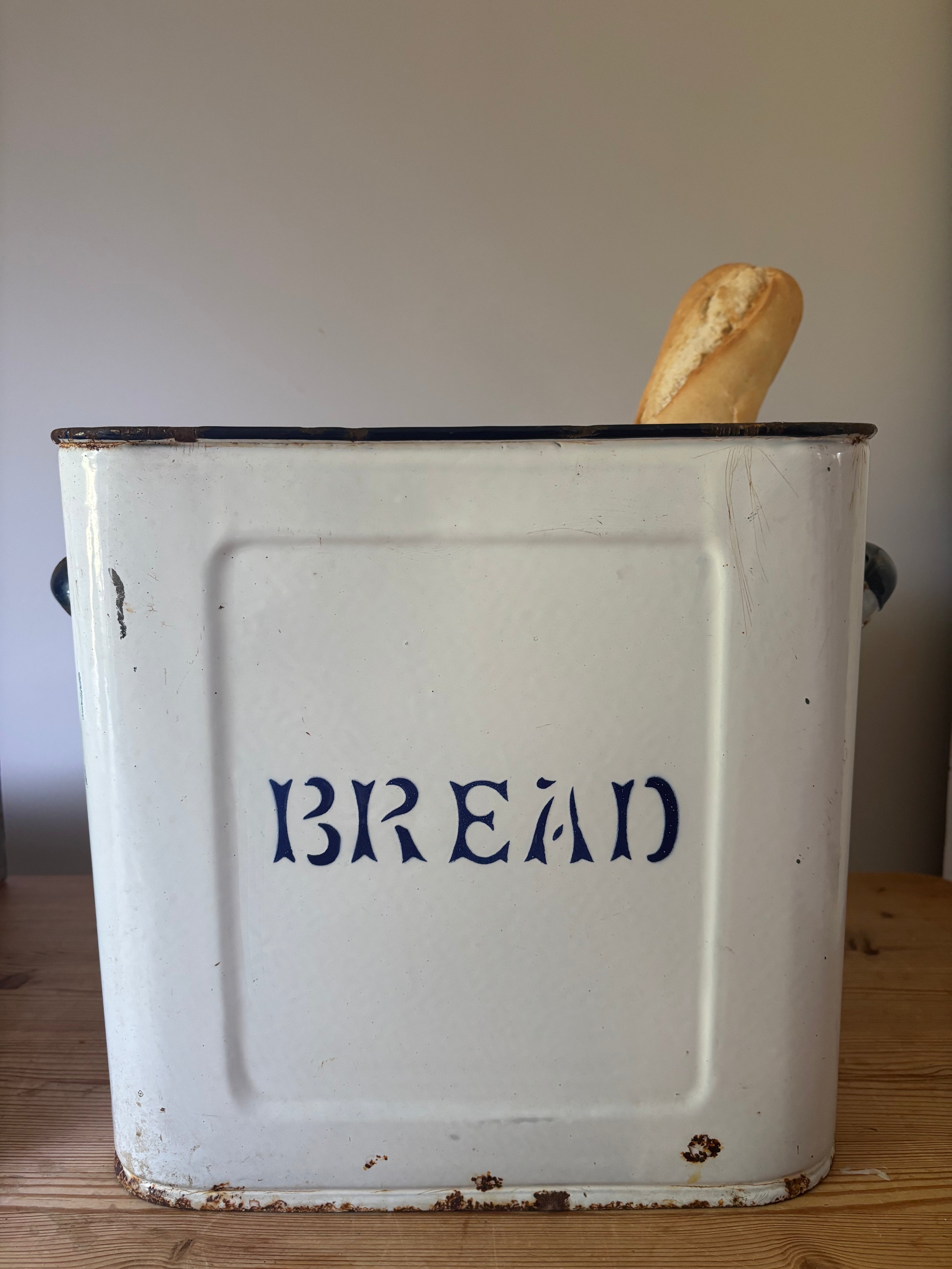 A vintage white enamel bread bin with blue lettering that reads 'BREAD'.