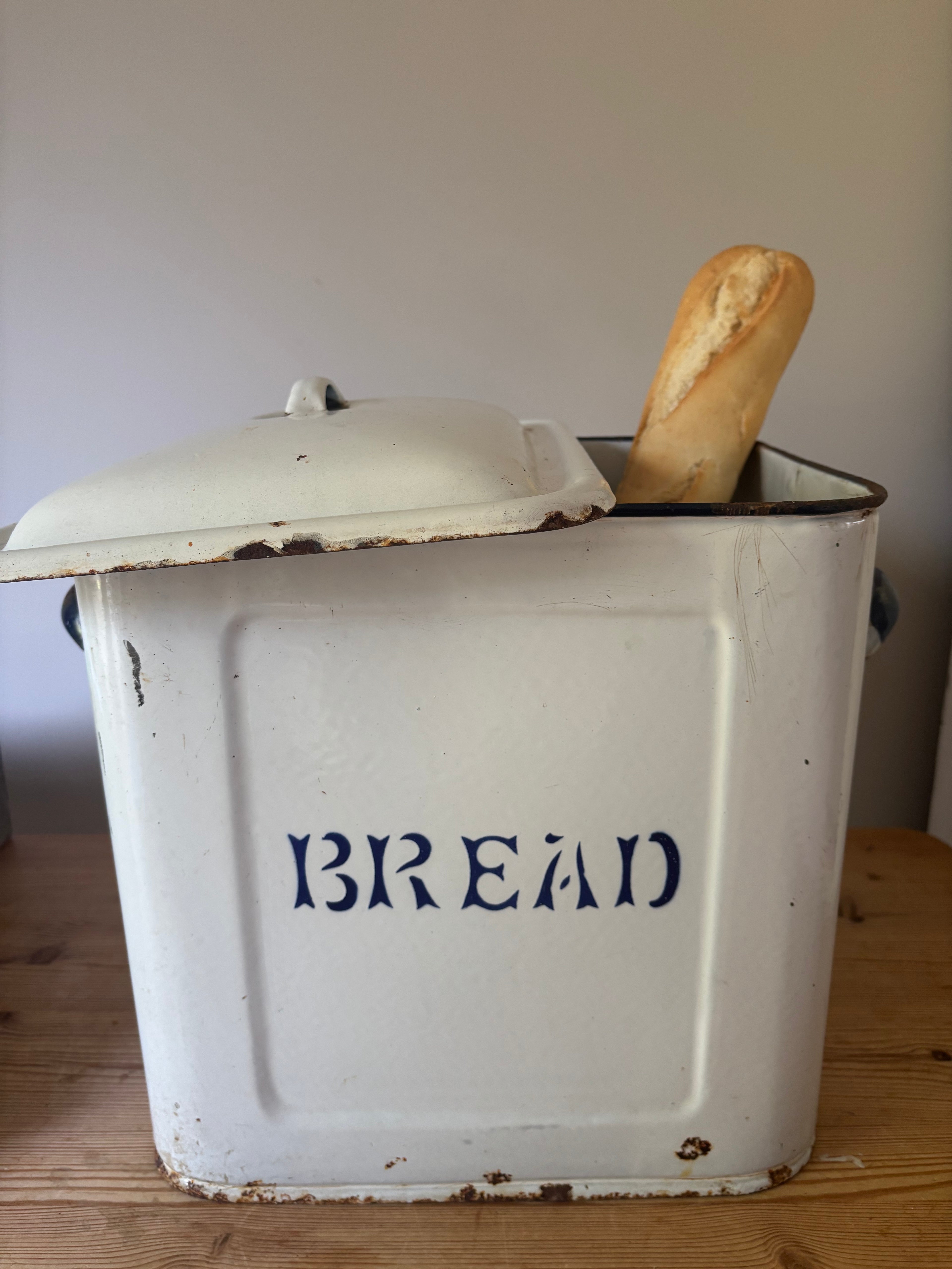 A vintage white enamel bread bin with a lid, featuring the word 'BREAD' in dark blue lettering.