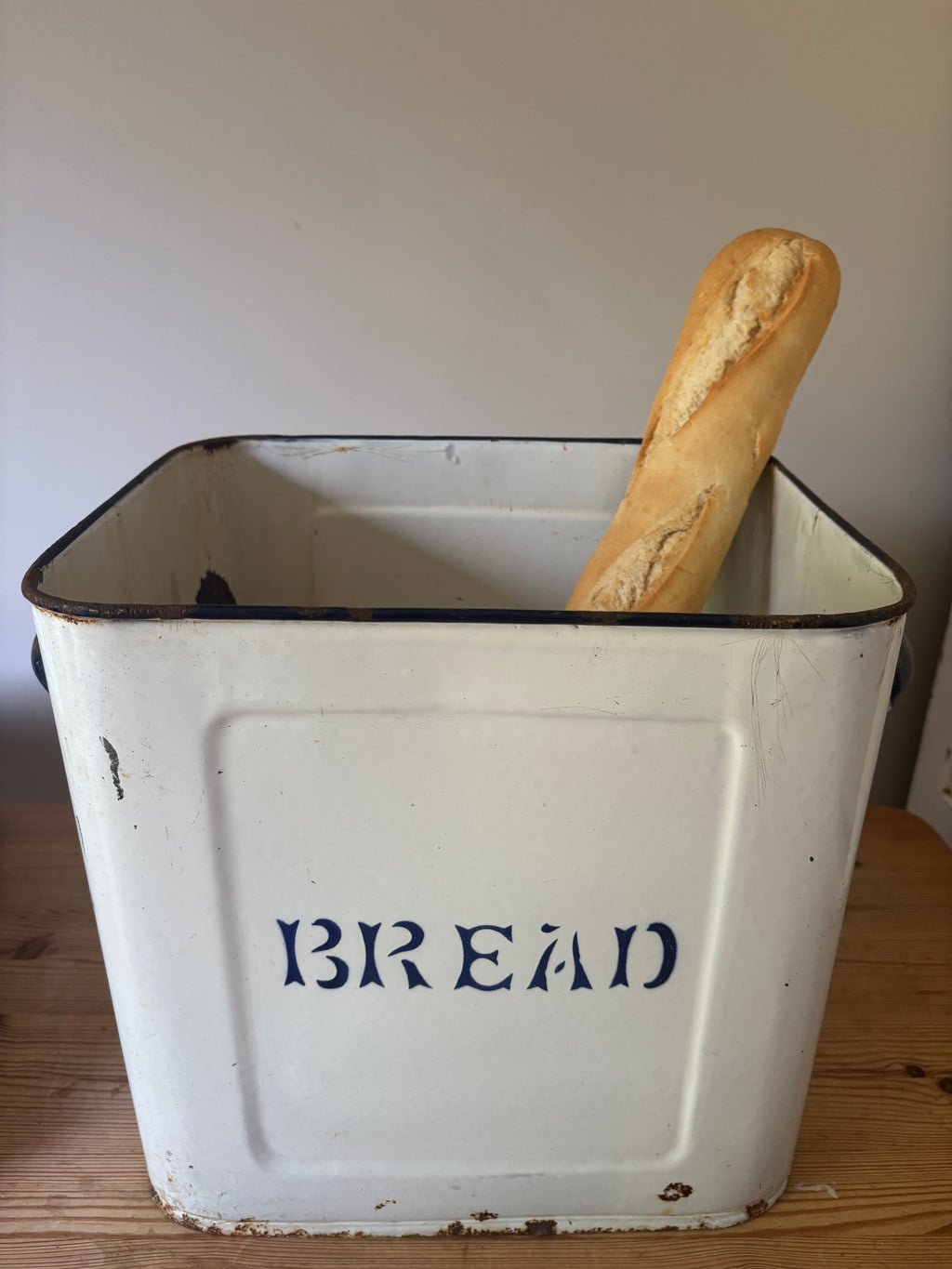 A vintage white enamel bread bin with 'BREAD' printed in blue on the front.