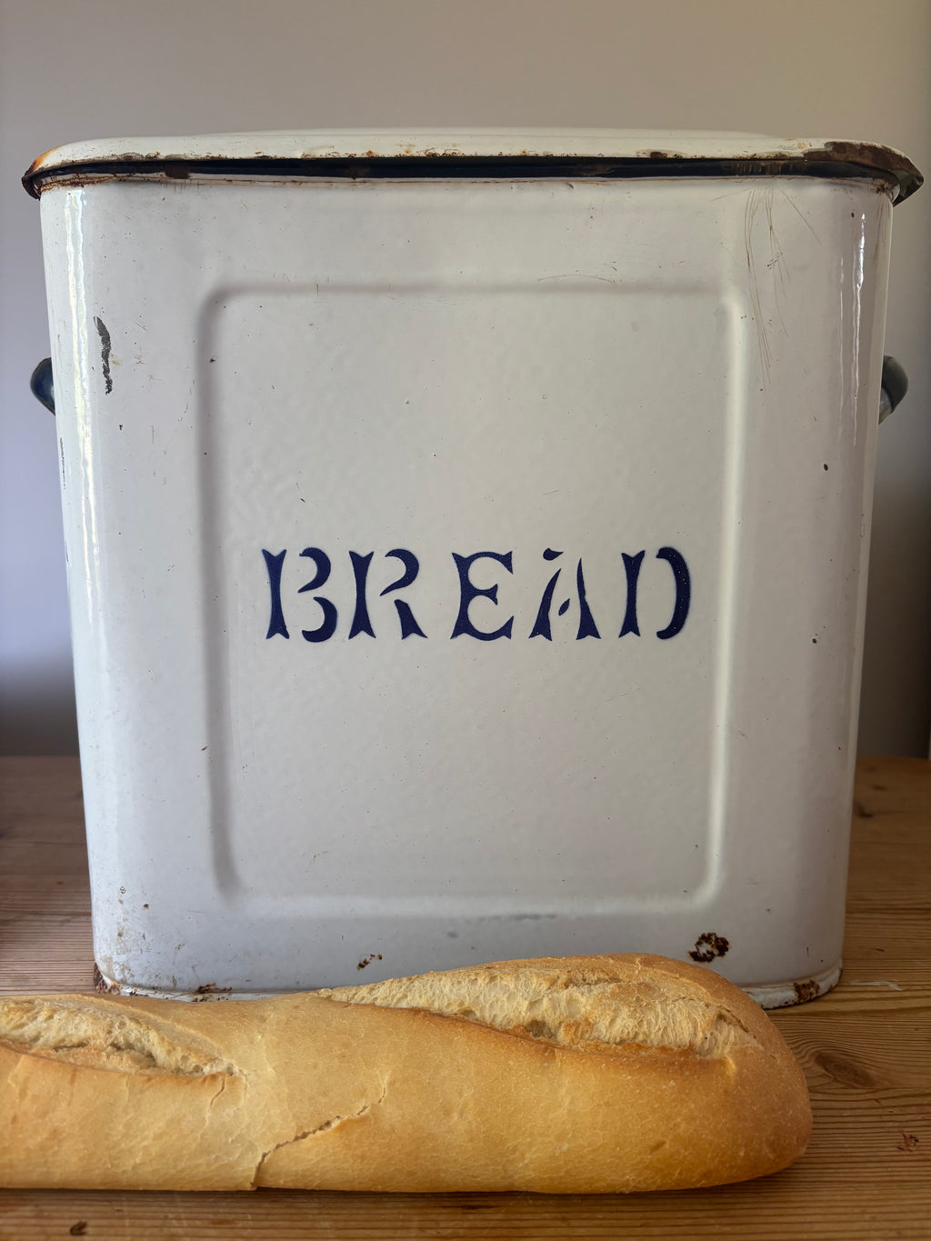 A vintage white enamel bread bin with 'BREAD' printed in dark blue letters.