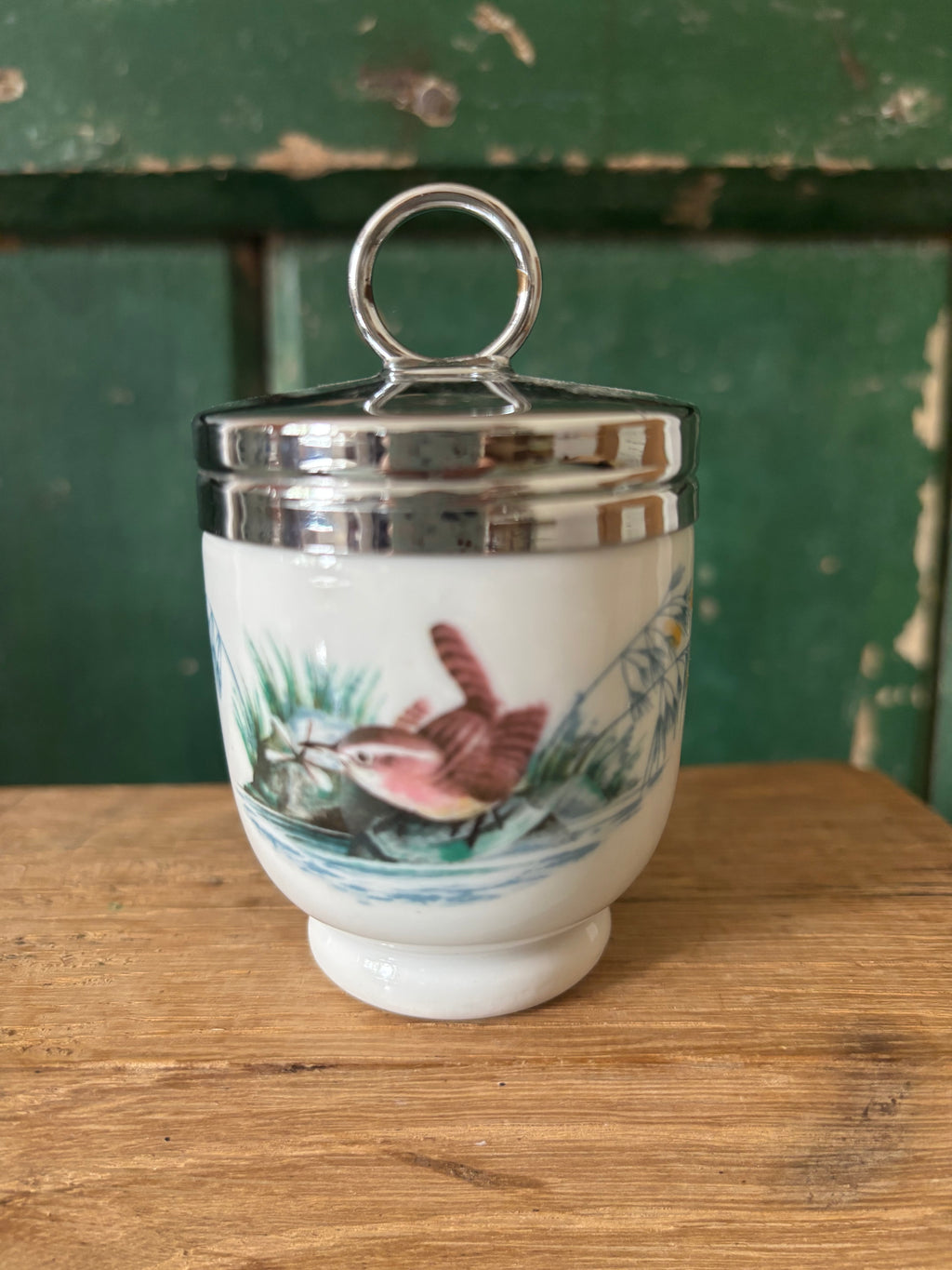 A vintage white ceramic lidded egg coddler with a silver metal lid and handle, decorated with a hand-painted bird transfer.