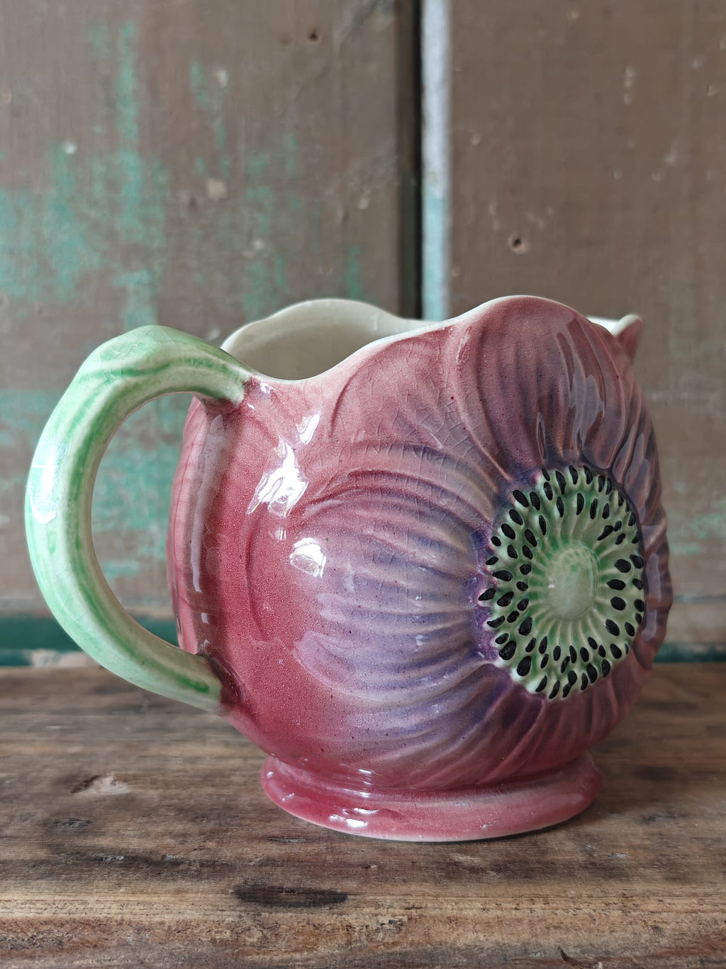 A hand painted ceramic jug shaped like a large anemone flower with a green handle.