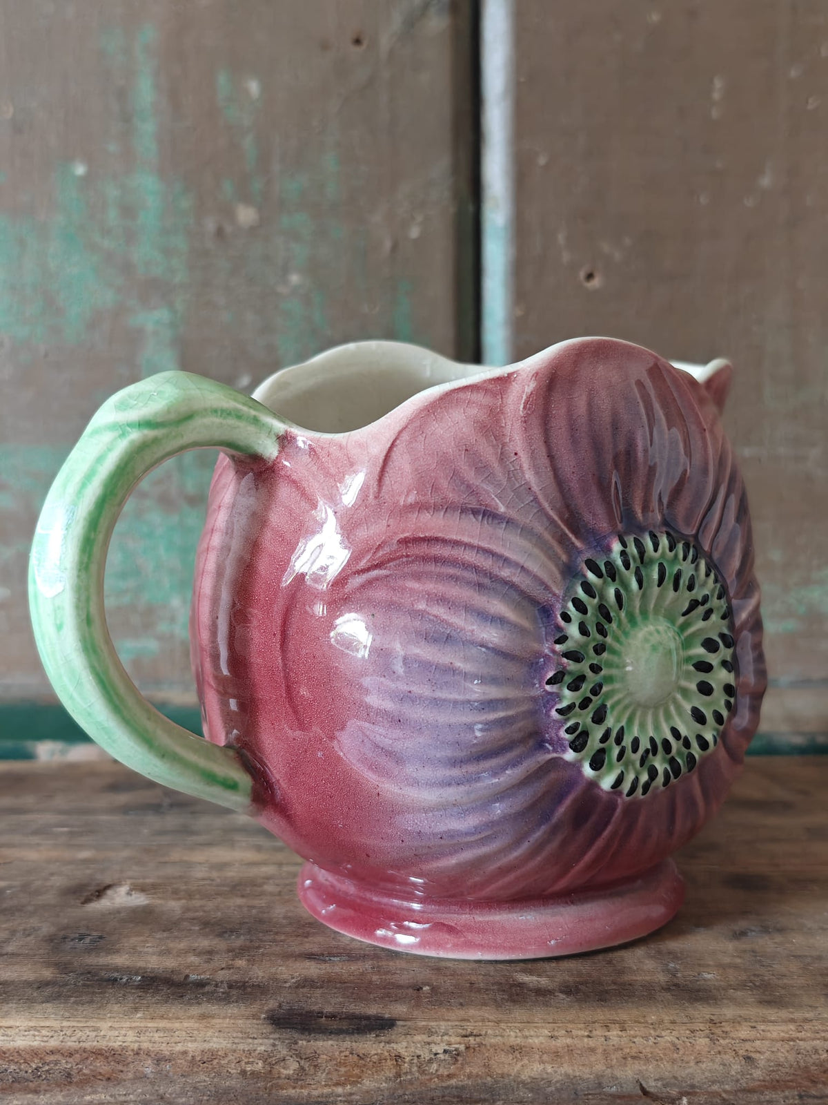 A hand painted ceramic jug shaped like a large anemone flower with a green handle.