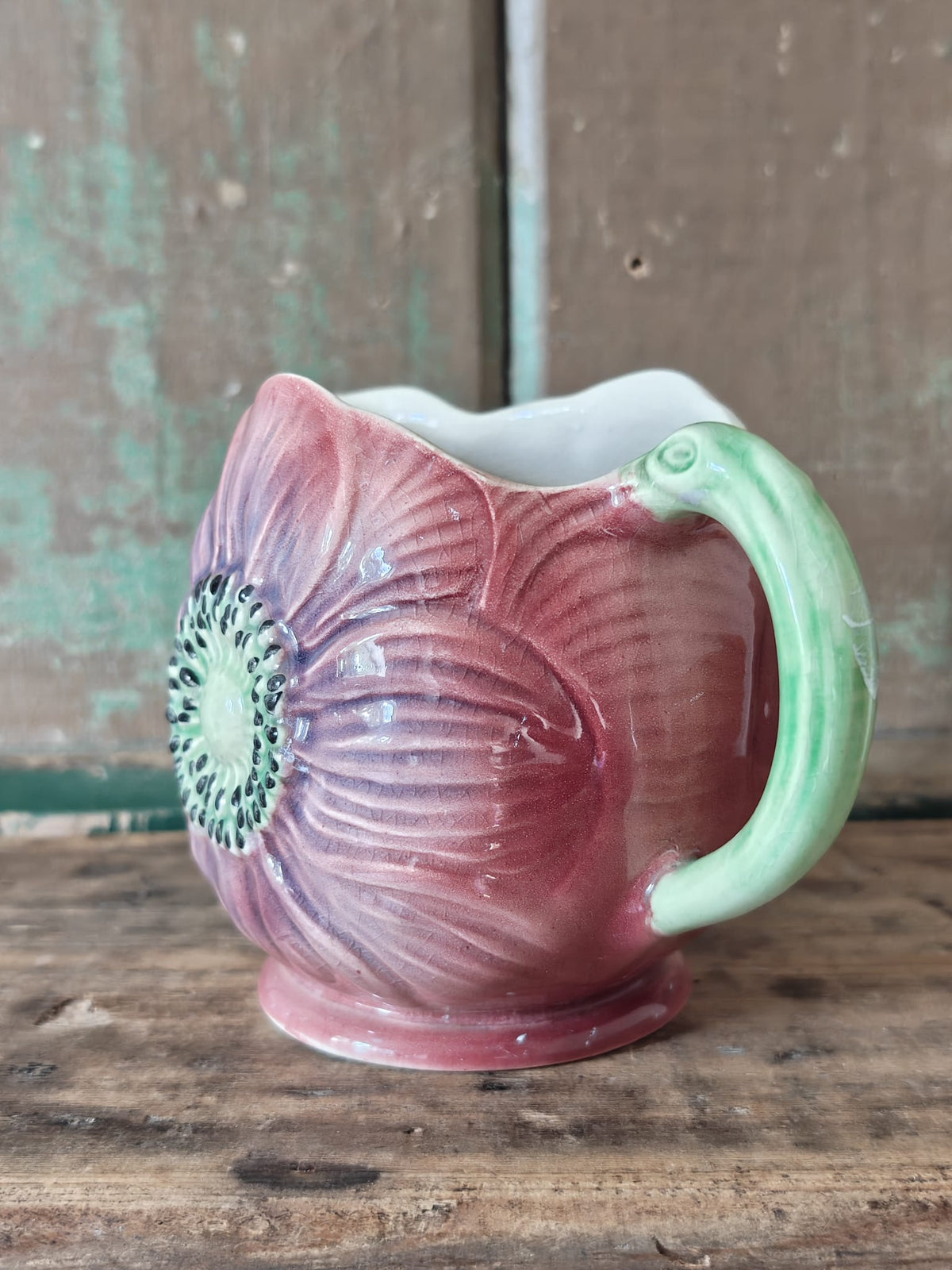 A vintage ceramic flower-shaped jug with a pink and purple glazed body.