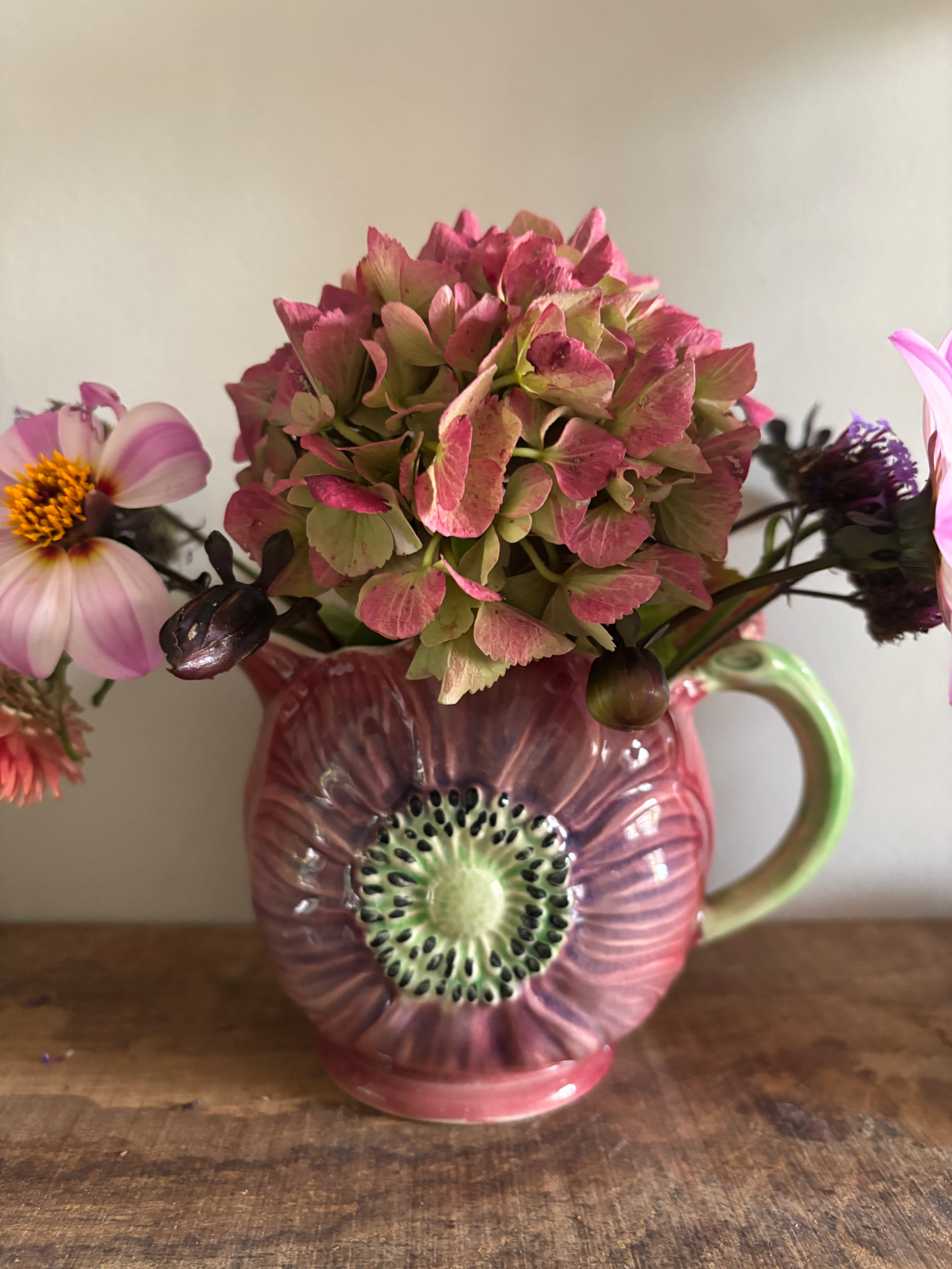 A purple ceramic jug with a green handle and floral relief detail.