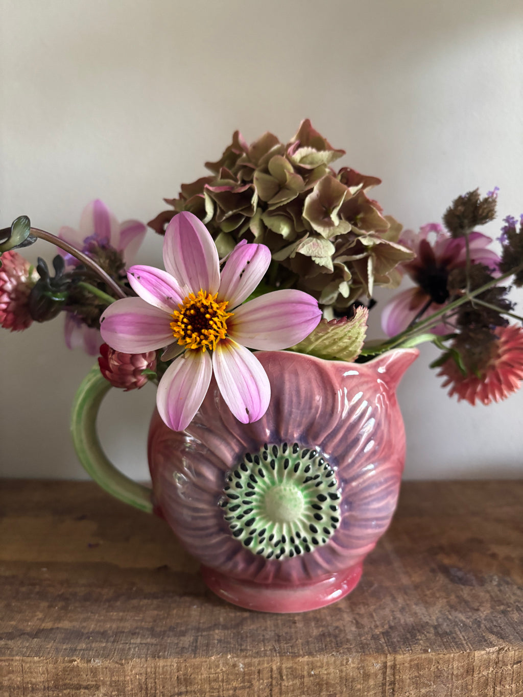A pink ceramic flower-shaped jug with a green handle and center detail.