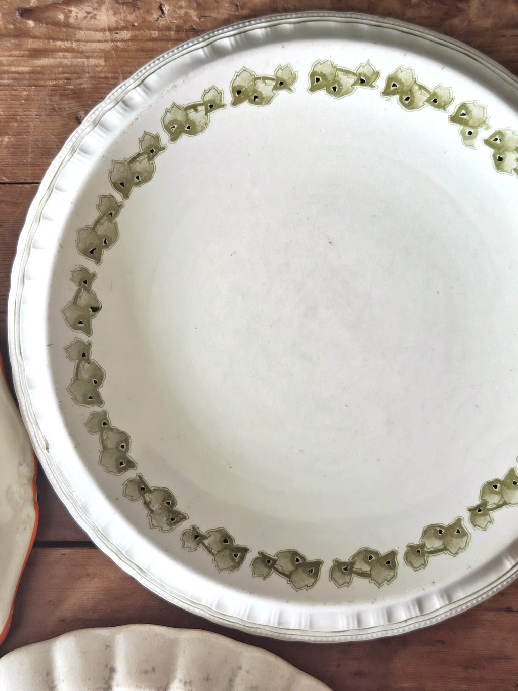 A white ceramic plate with a scalloped rim decorated with green leaves.