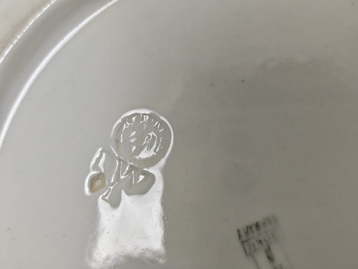 Close-up of the underneath of a white ceramic plate  showing a circular embossed logo.