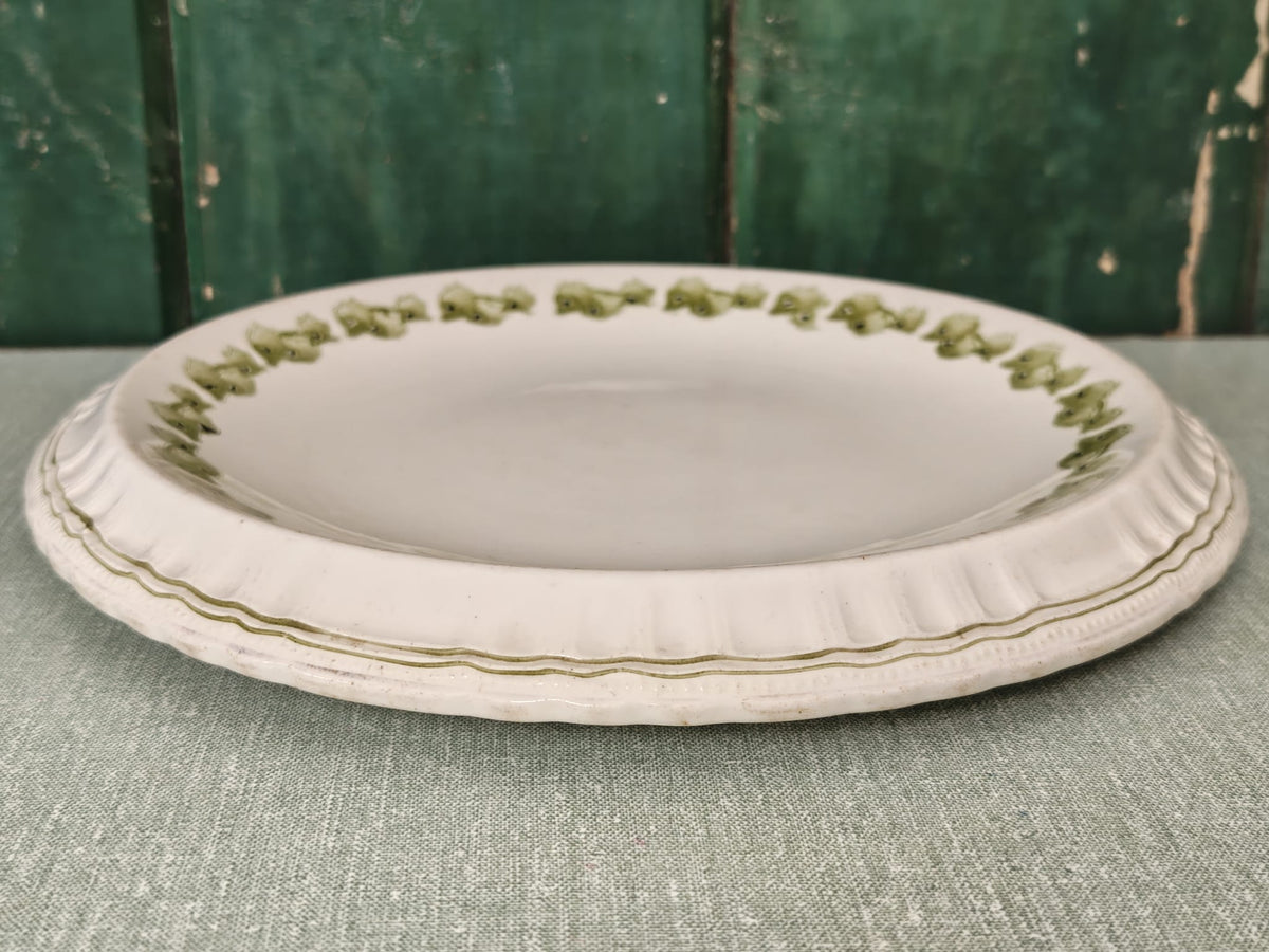 A round white ceramic plate with a scalloped rim and a delicate green leaf pattern around the edge.