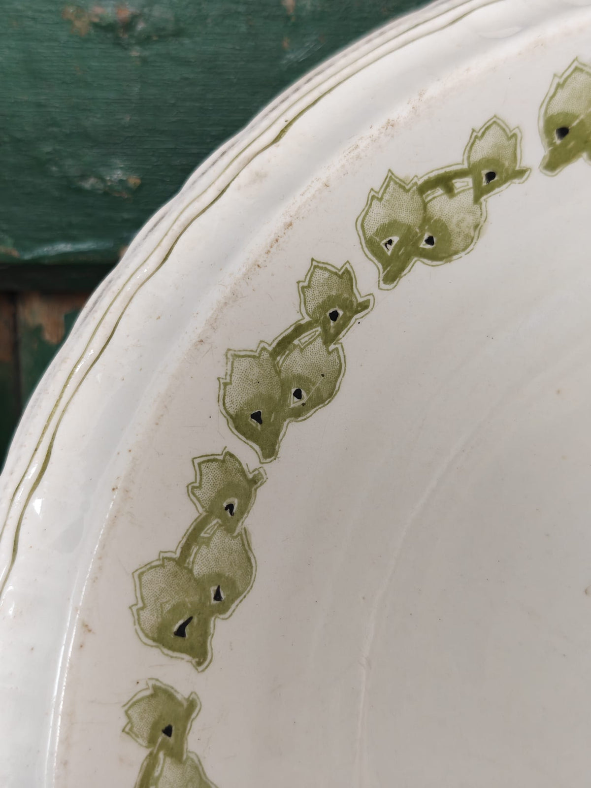 Close-up of a white ceramic plate featuring a decorative border of olive green stylized leaf.