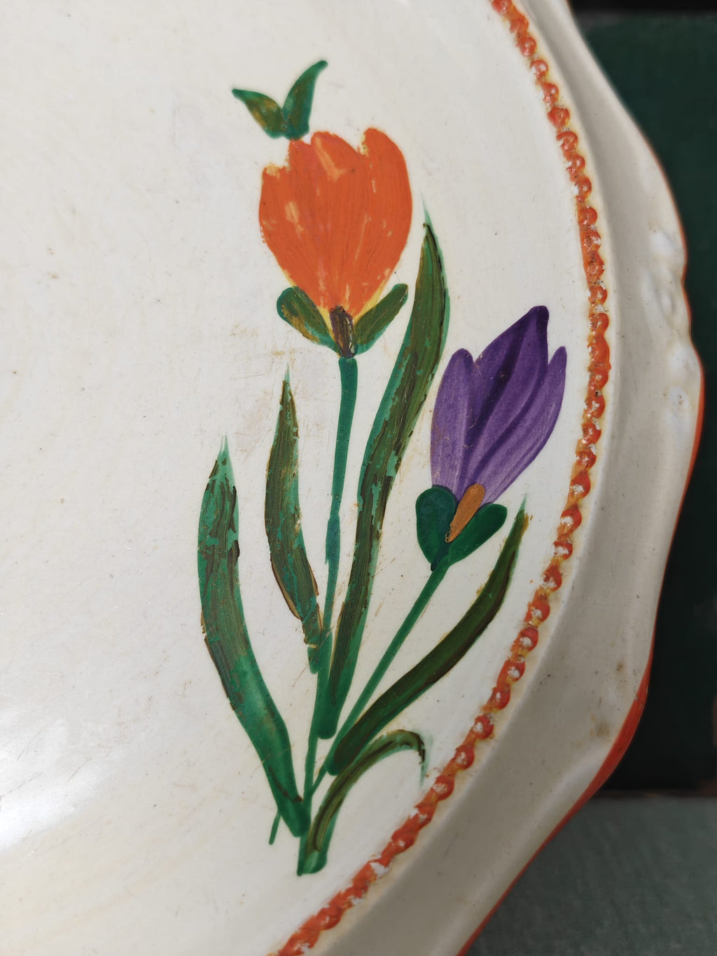 Close-up of a white ceramic plate with a hand-painted design featuring an orange tulip, a purple crocus, green leaves, and a decorative orange border.