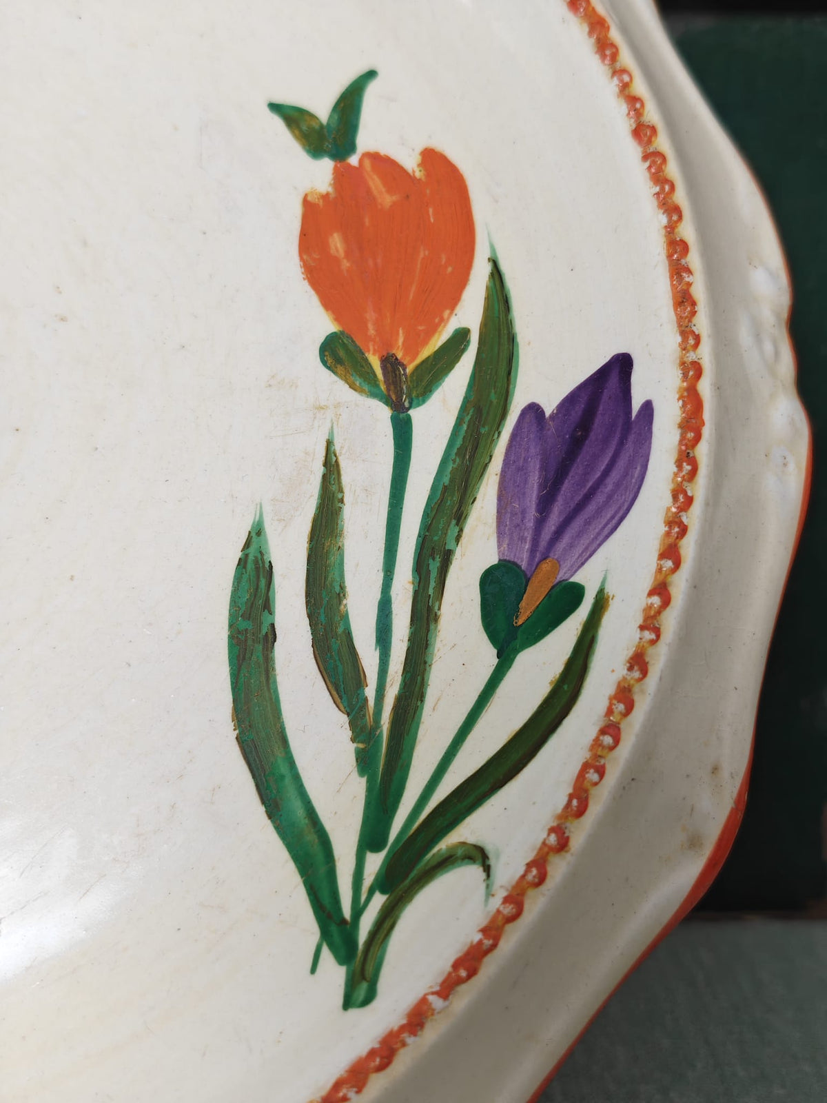 Close-up of a white ceramic plate with a hand-painted design featuring an orange tulip, a purple crocus, green leaves, and a decorative orange border.