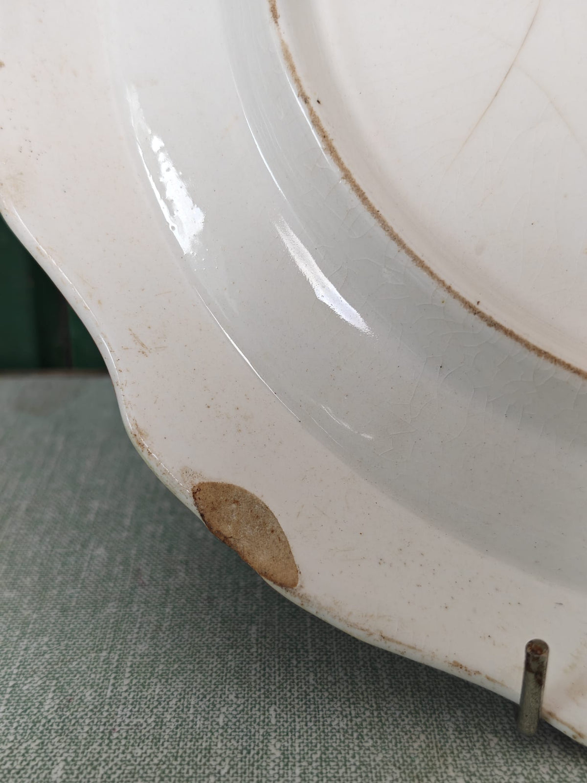 Close-up of a white ceramic plate with a scalloped rim, showing a small brown stain or chip near the edge,