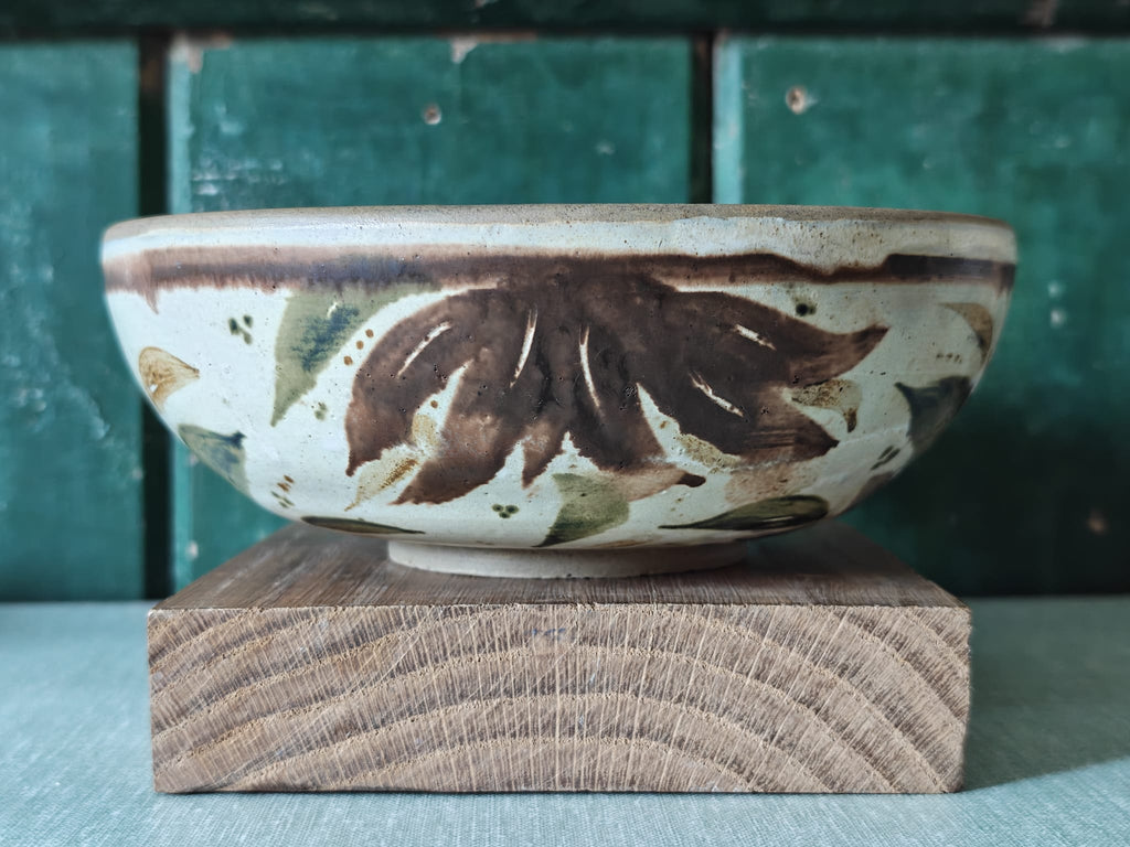 A handmade ceramic bowl with a rustic hand-painted leaf pattern in brown and muted green on an off-white glaze.
