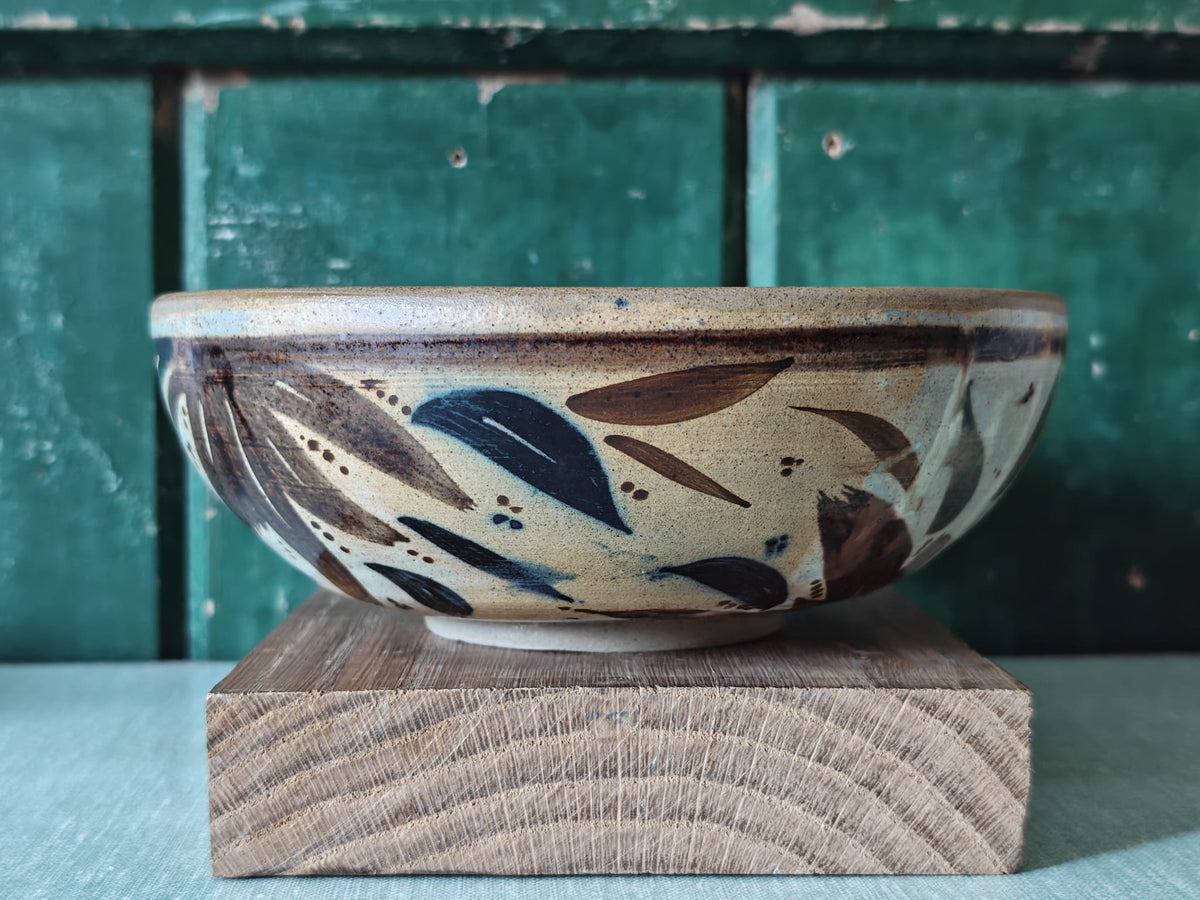A handmade ceramic bowl with a speckled beige glaze and hand-painted leaf patterns.