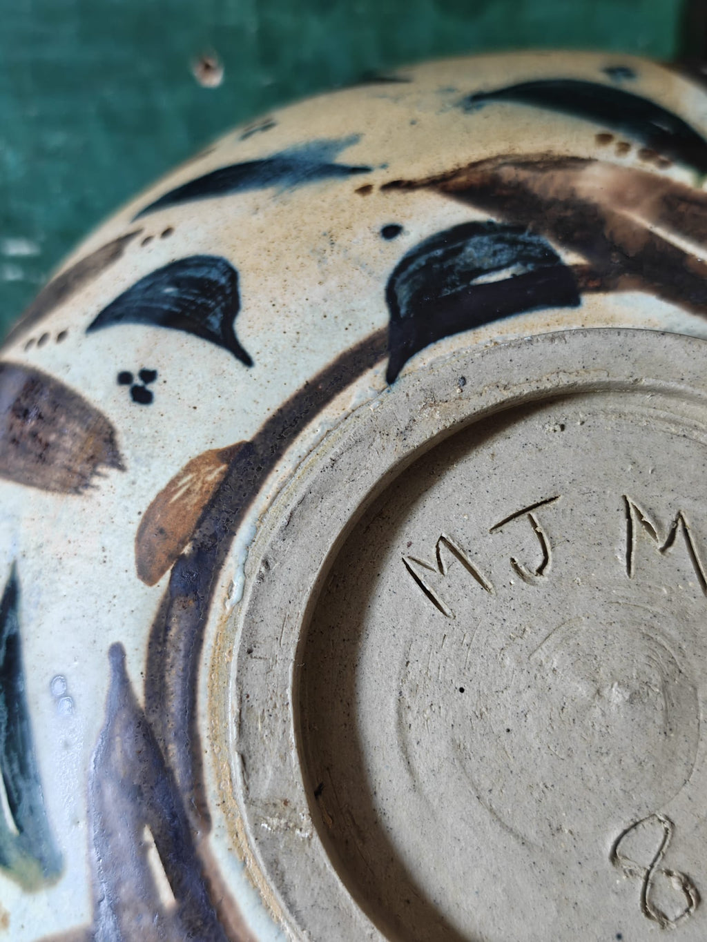 Close-up of the base of a handmade ceramic bowl, showing the interior foot ring stamped with 'MJ M' .