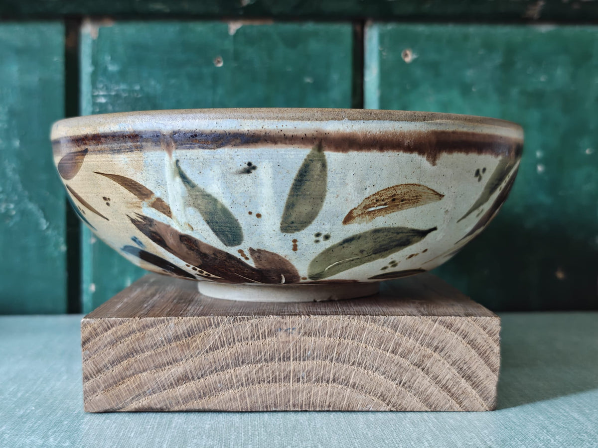 A handmade ceramic bowl with a rustic hand-painted leaf pattern in earthy brown, olive green, and beige tones.