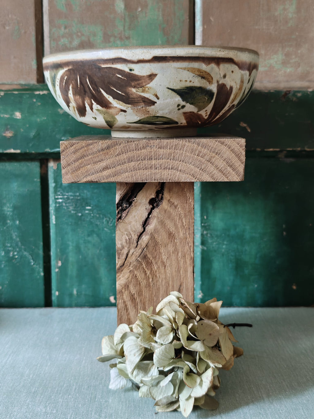 A handmade ceramic bowl with a brown and green leaf pattern on a cream background.