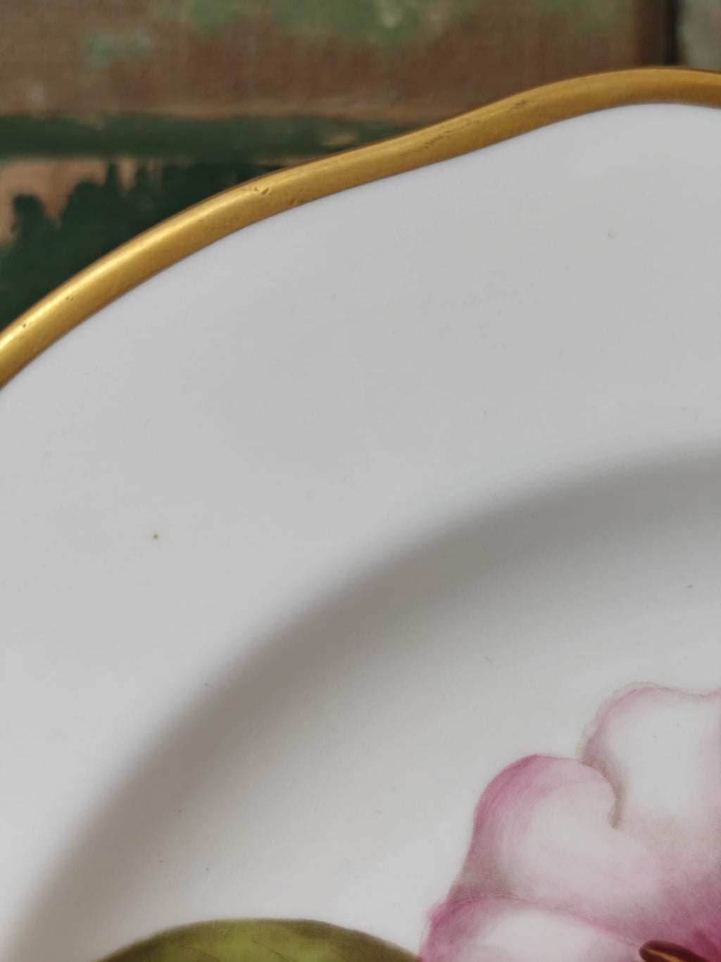 Close-up detail of a white ceramic plate with a scalloped gold rim and a pink floral decoration in the lower right corner.