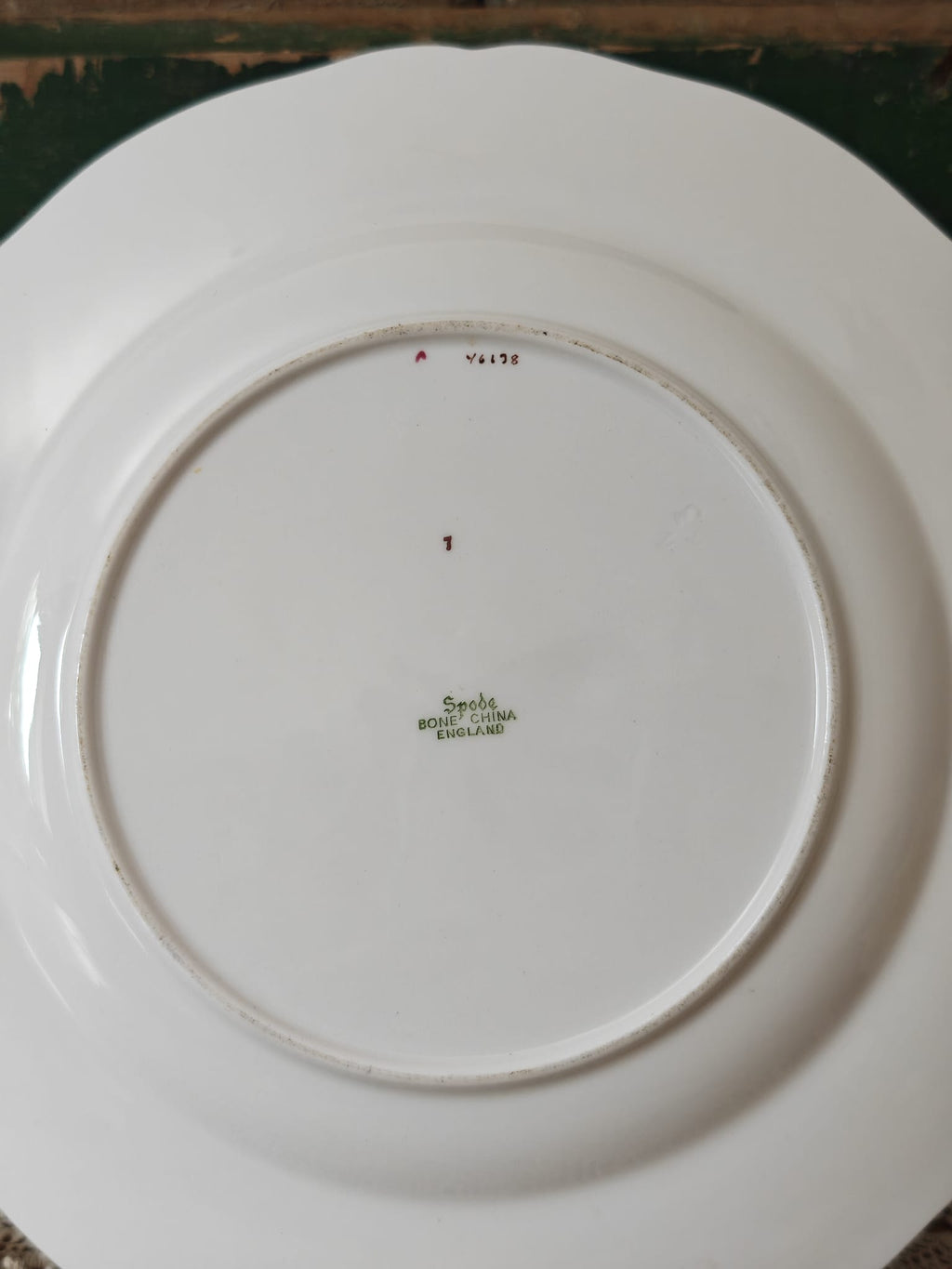 The underside of a white ceramic plate with a scalloped rim, showing a green printed maker's mark.