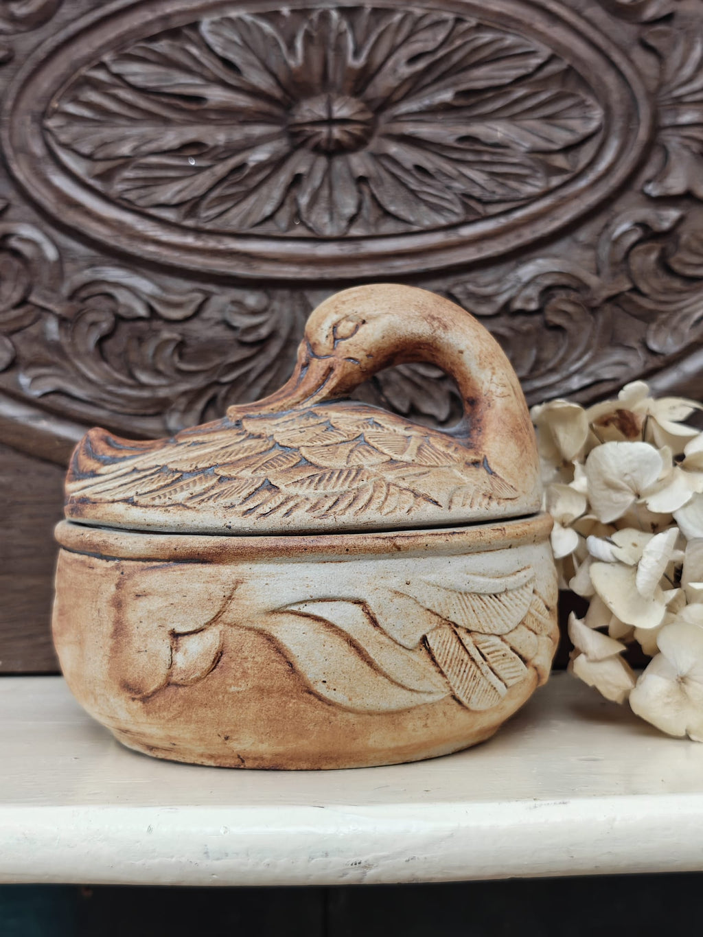 A small carved ceramic duck-shaped lidded dish in a warm tan and brown glaze.