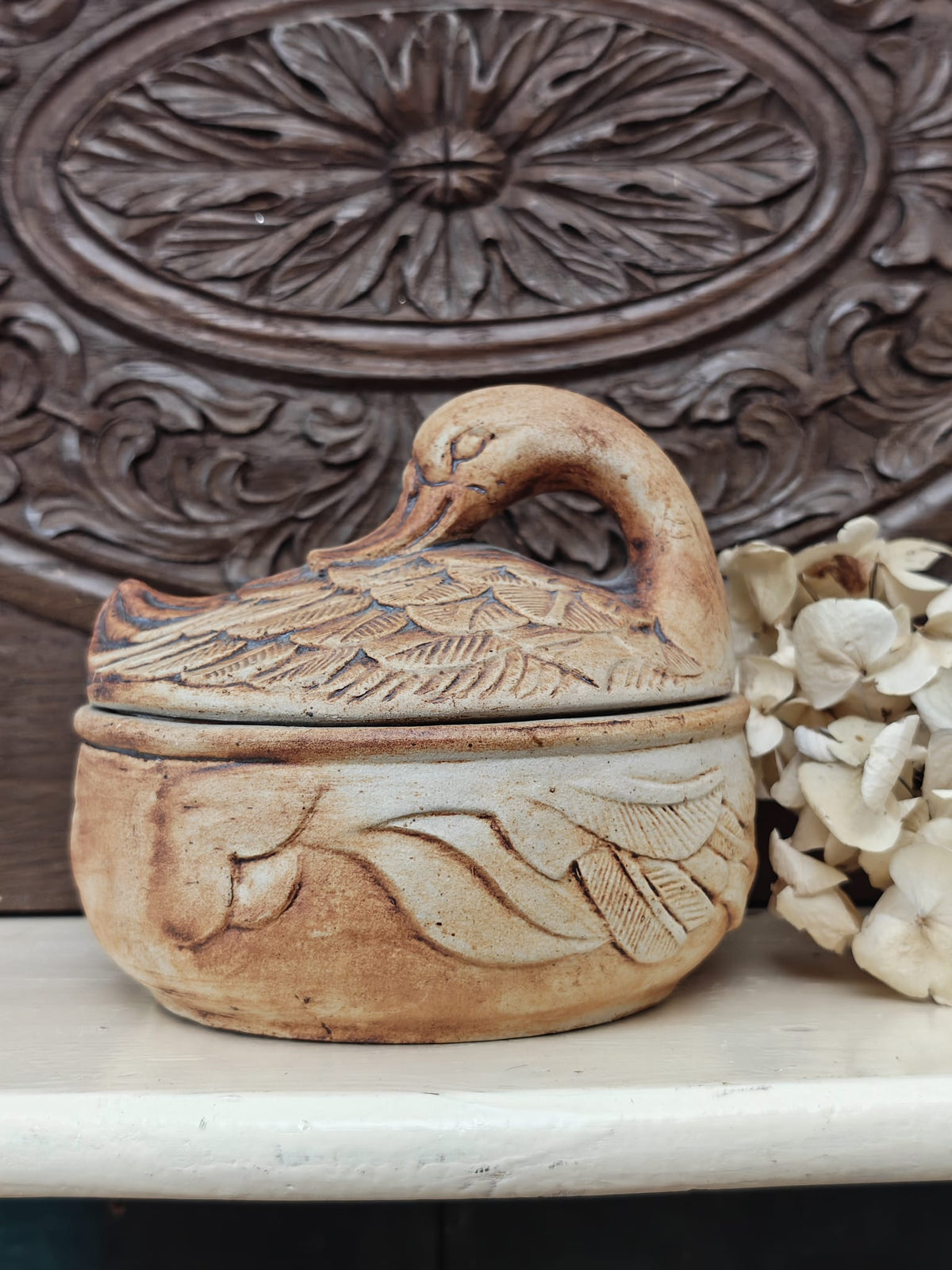 A small carved ceramic duck-shaped lidded dish in a warm tan and brown glaze.