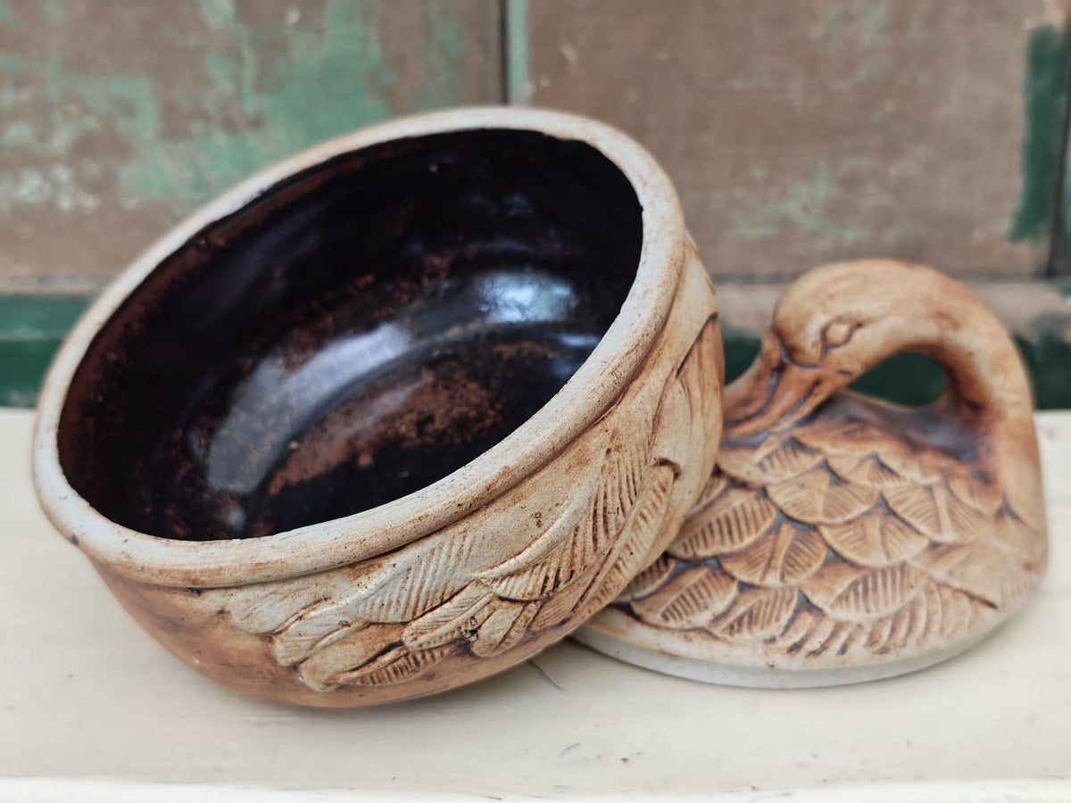 A rustic handmade ceramic duck shaped bowl with a dark glazed interior and carved feather details on the exterior.