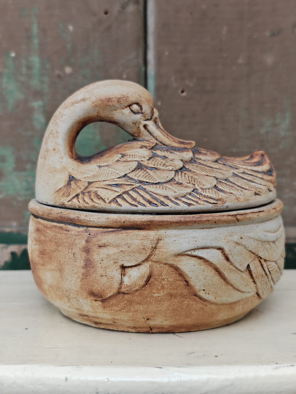 A rustic ceramic duck-shaped lidded dish with carved feather and leaf details.