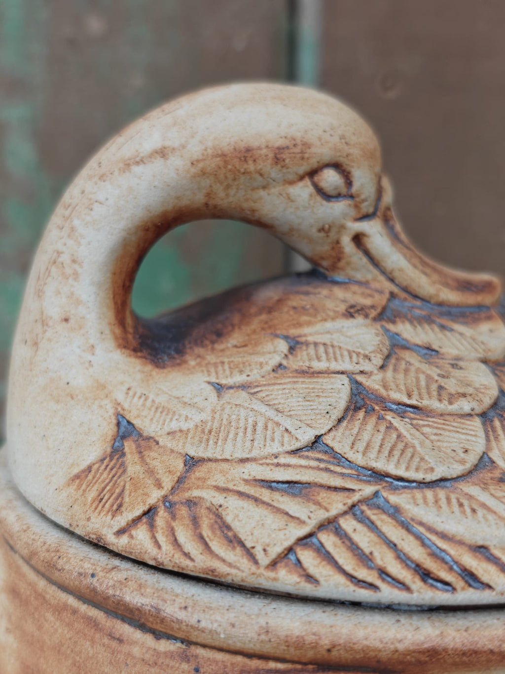 Close-up of a ceramic duck-shaped container lid with carved feather details and a rounded body.