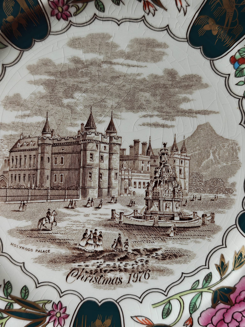 A close-up of a decorative ceramic plate featuring an engraved sepia-toned scene of Holyrood Palace in Edinburgh and the text 'Holyrood Palace Christmas 1976.
