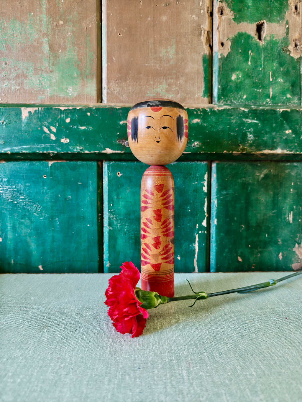 Wooden kokeshi doll with red floral patterns 