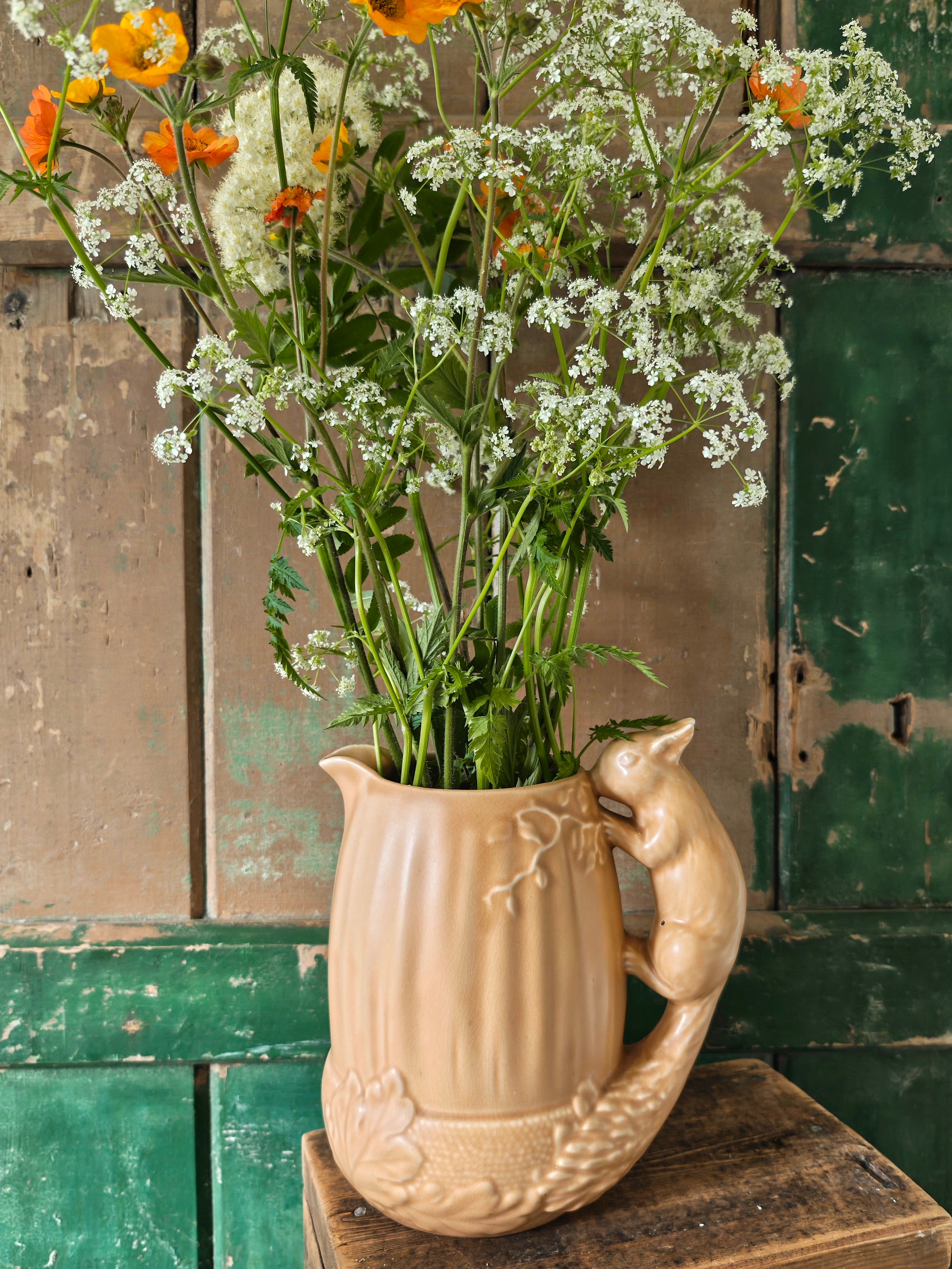 Brown ceramic pitcher in acorn shape with a squirrel design handle displayed with flowers