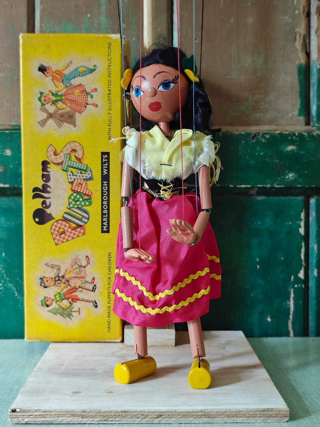 Traditional marionette puppet with a yellow box featuring illustrations of similar puppets in the background.