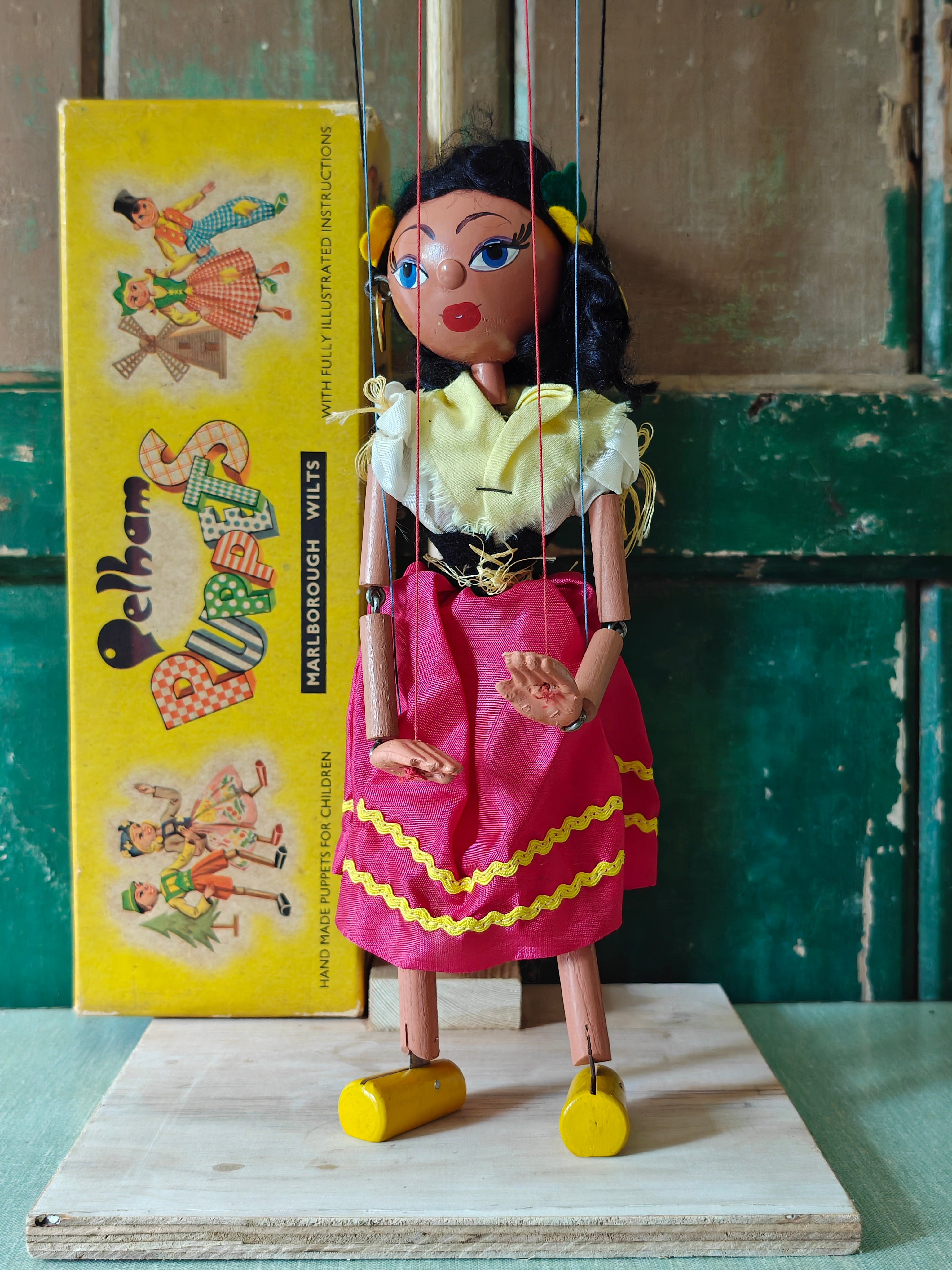 Traditional marionette puppet with a yellow box featuring illustrations of similar puppets in the background.