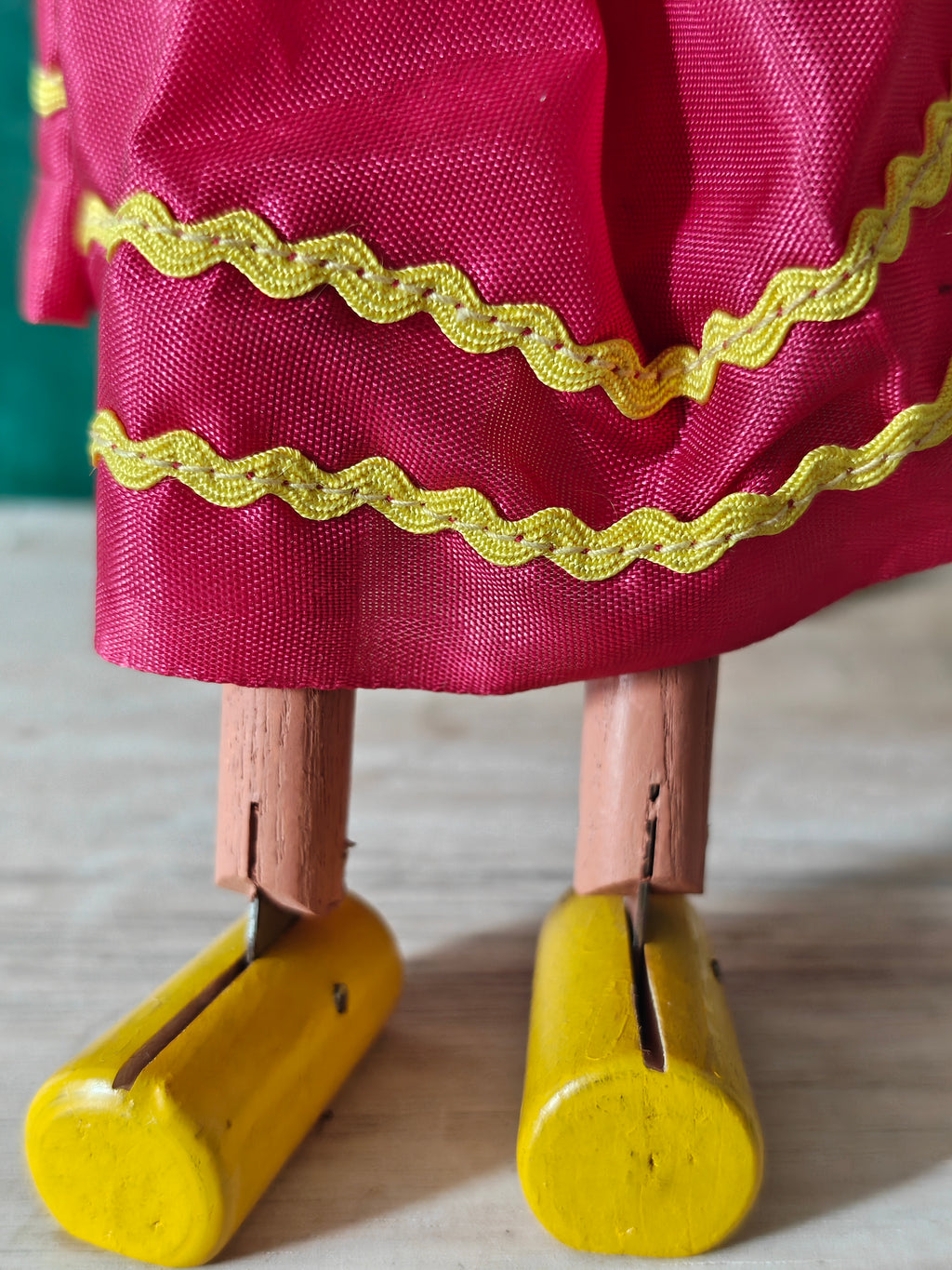 Wooden puppet with pink cloth and yellow trim with yellow wooden feet
