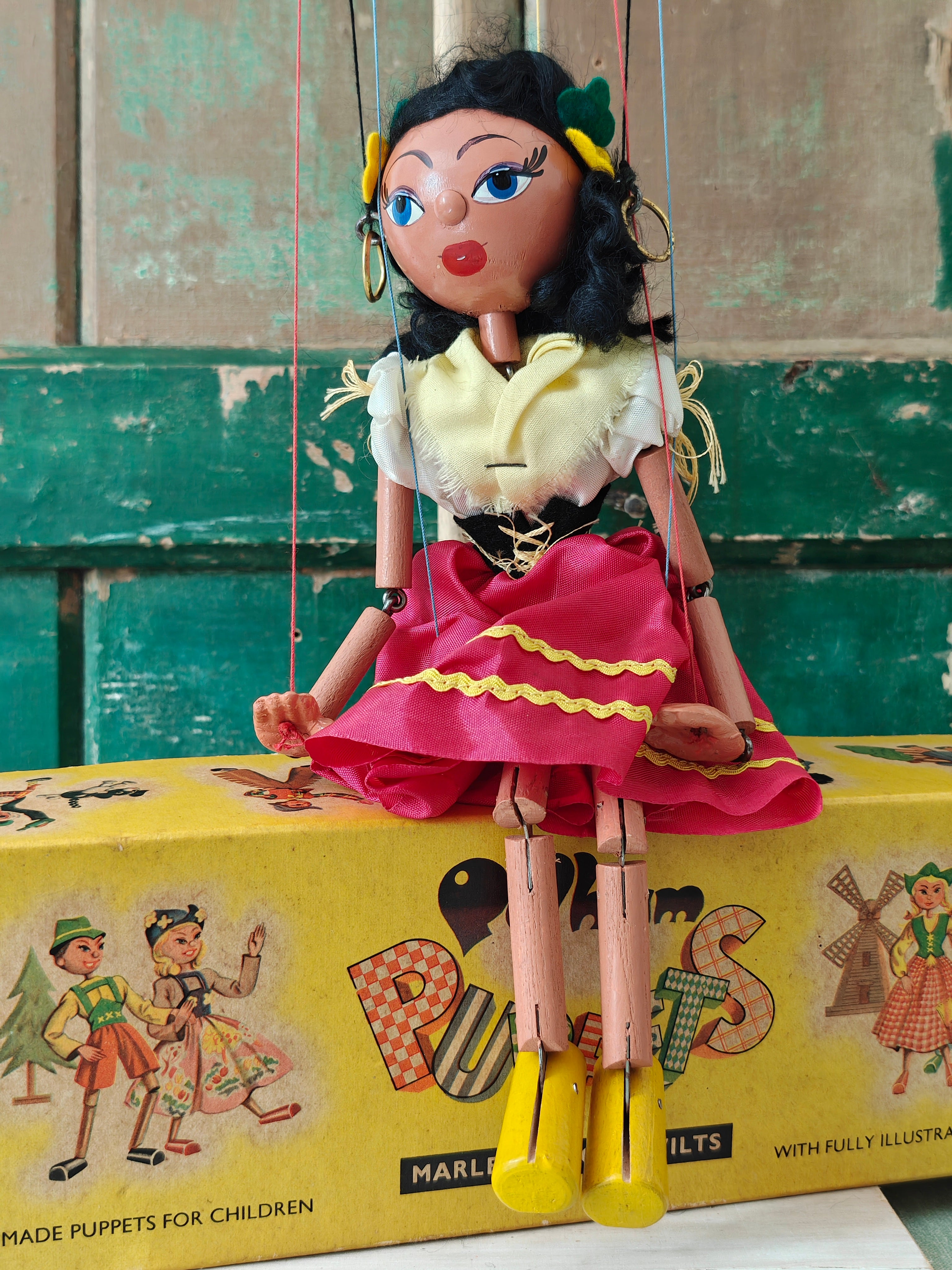 Marionette puppet with a colorful dress on top of a vintage puppet box.